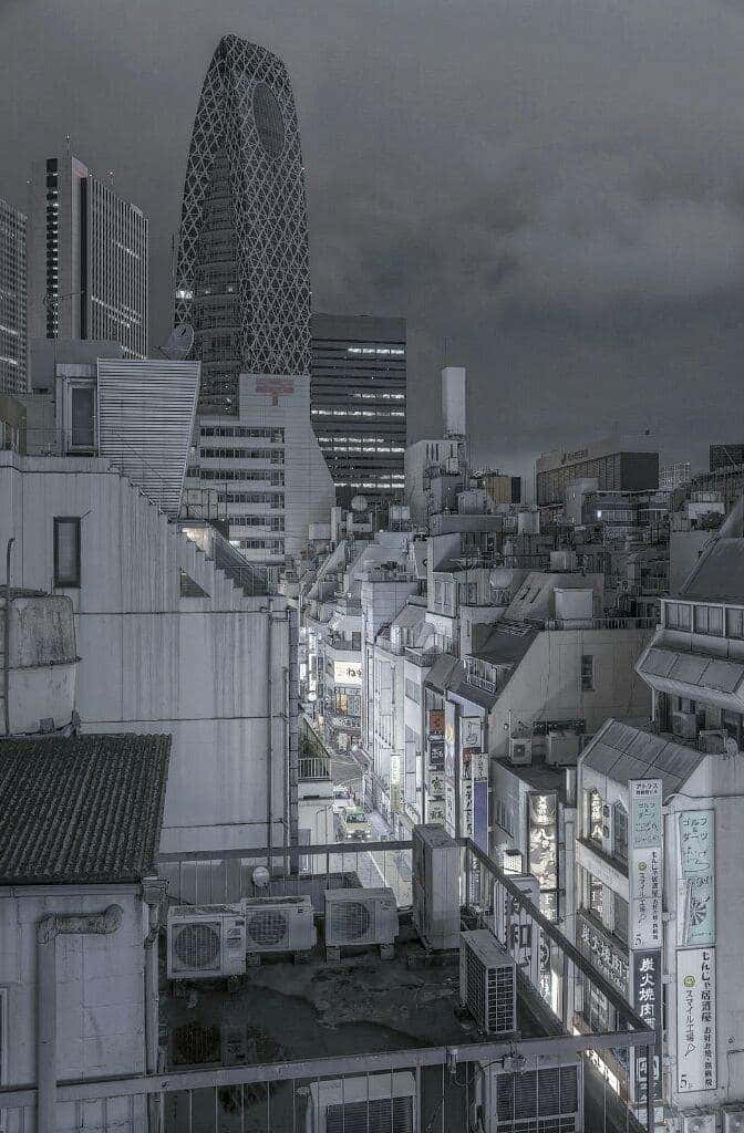 沉醉於柔和灰色美學的寧靜與自由 壁紙 — 陰鬱的黑白城市夜景，密集建築物上方聳立著格子狀摩天大樓，街燈閃爍。