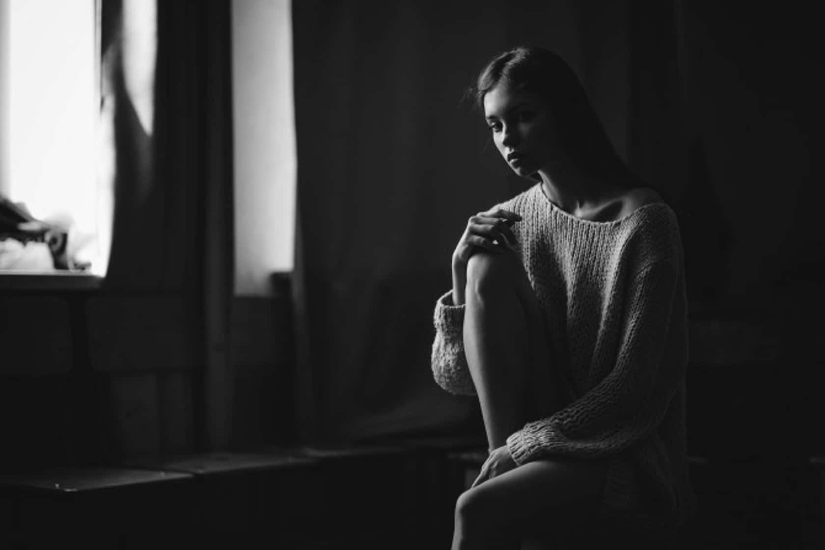 穿著針織毛衣的女性坐在昏暗房間的窗邊