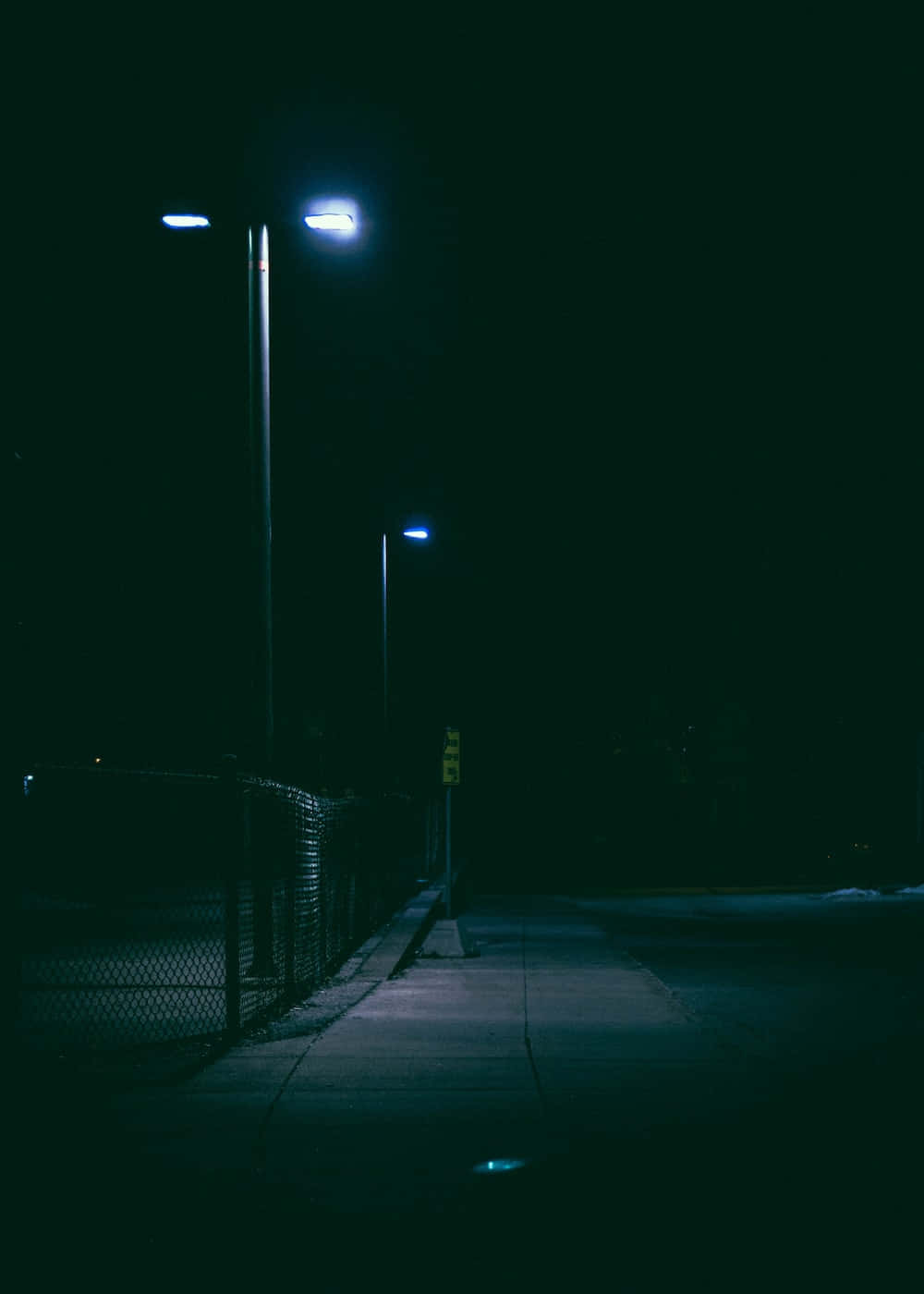 夜晚一條安靜的城市人行道，被藍色路燈和鐵絲網照亮。