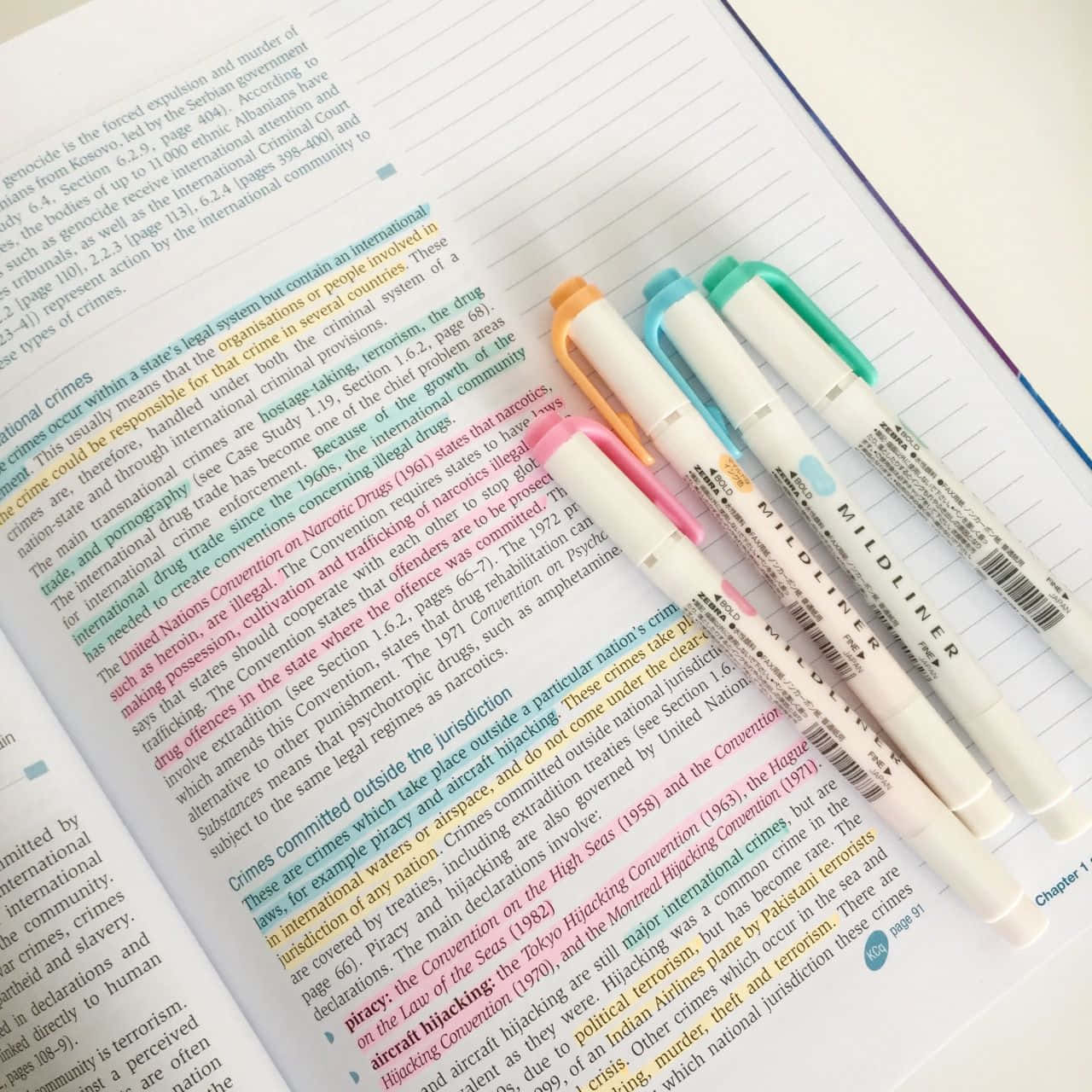 沉醉於自然之美 壁紙 — 四支色彩繽紛的Mildliner螢光筆放在一本打開的教科書頁面上，頁面有被標示的法律文字。