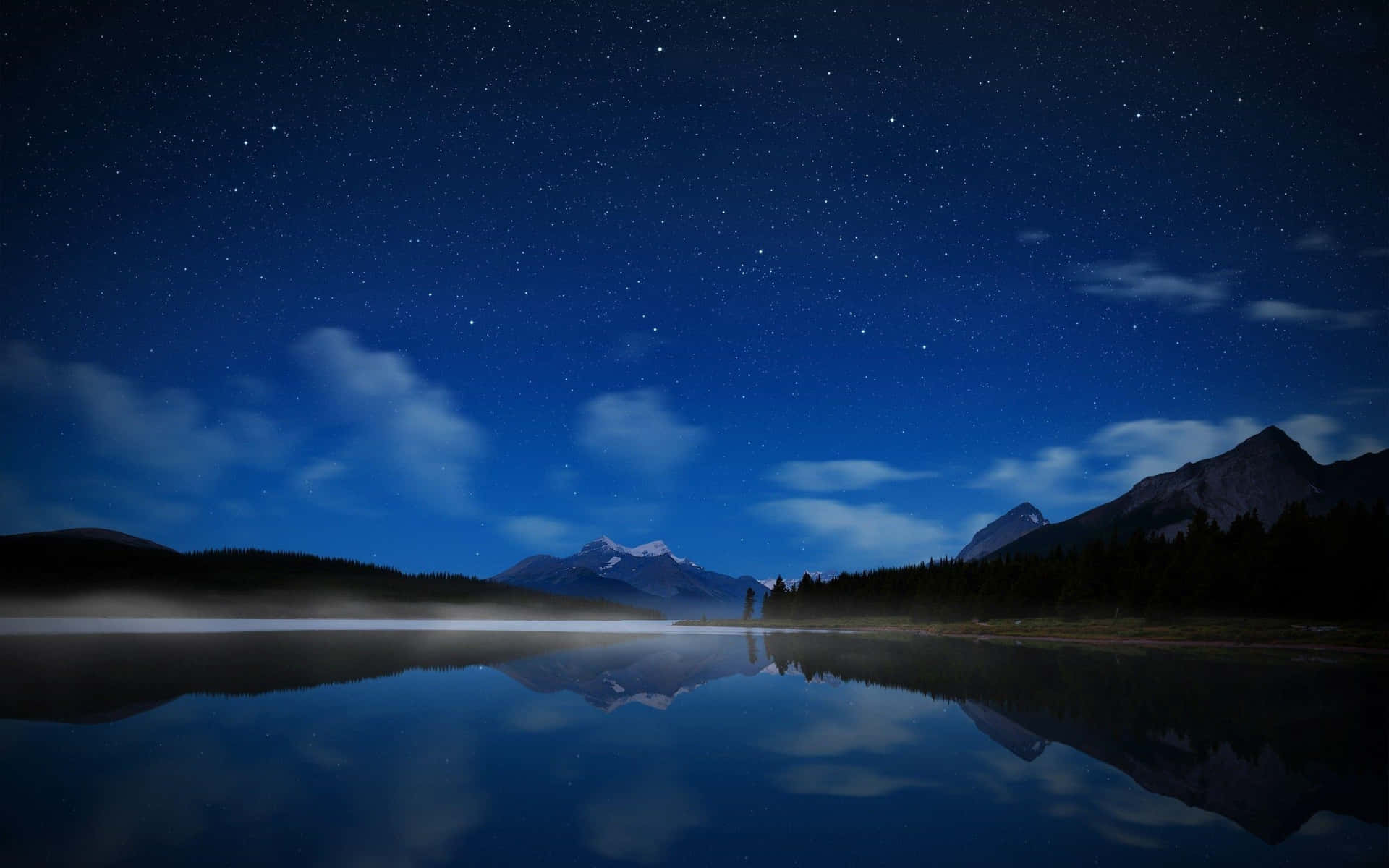 繁星點點的夜空倒映在平靜的湖面上，背景有山脈。