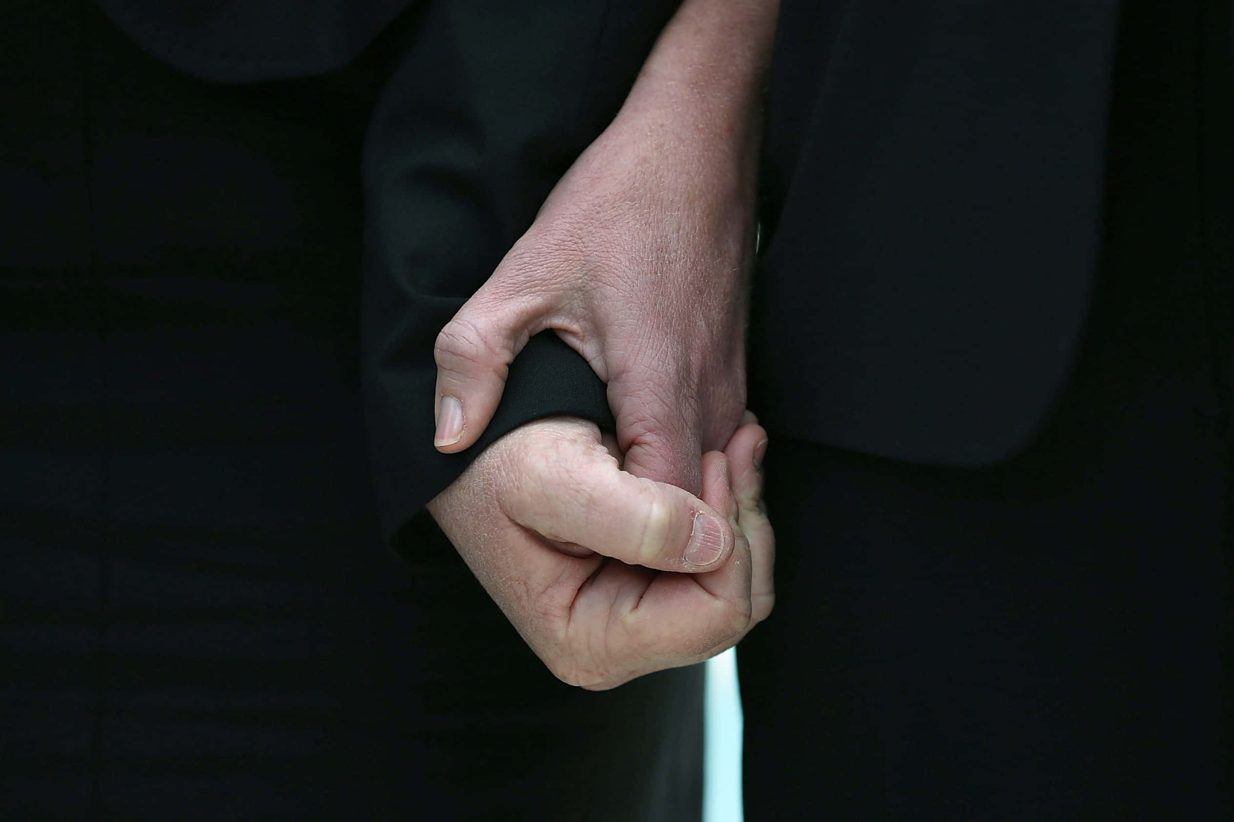 沒有什麼比與所愛之人牽手更令人感動 壁紙 — 兩隻手緊緊握在深色西裝袖中，傳達深刻的情感支持和親密感。
