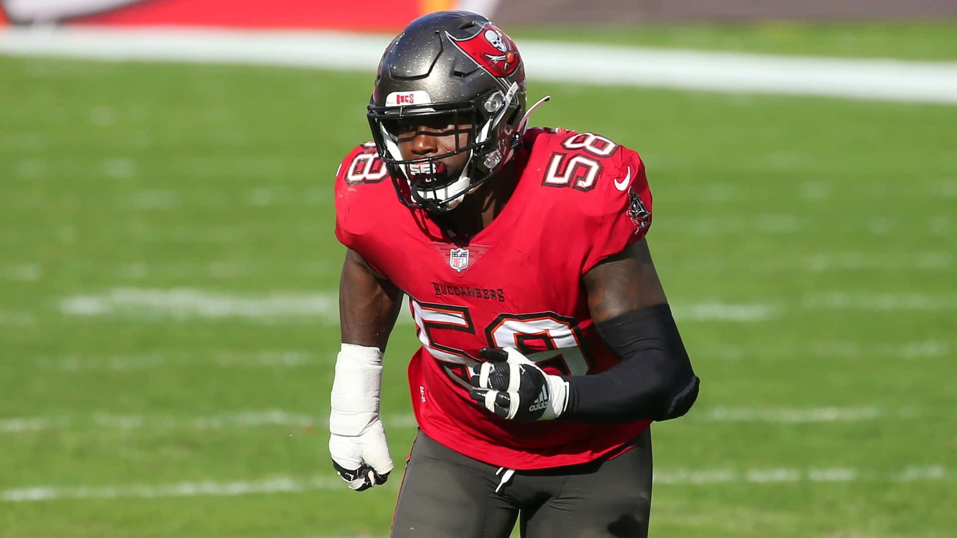 沙奎爾·巴雷特 NFL 球員後衛坦帕 壁紙 — 一名身穿紅色球衣的坦帕灣海盜隊美式足球員在陽光明媚的綠色球場上奔跑。