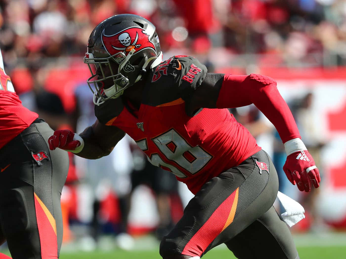 沙奎爾·巴雷特 坦帕 NFL 球員 壁紙 — 一名身穿紅黑色球衣的坦帕灣海盜隊美式足球員，在陽光普照的球場上動態衝刺，背景是模糊的體育場人群。