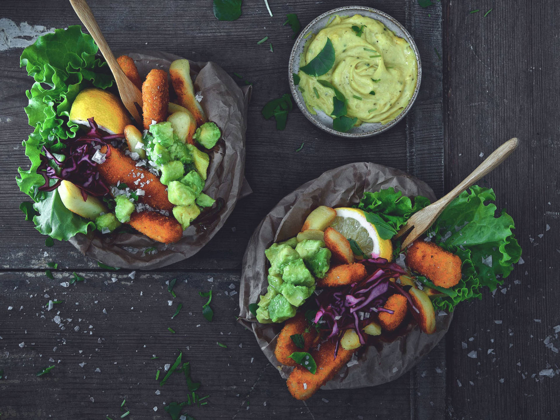 兩碗炸魚條配牛油果和椰菜，放在深色木桌上。