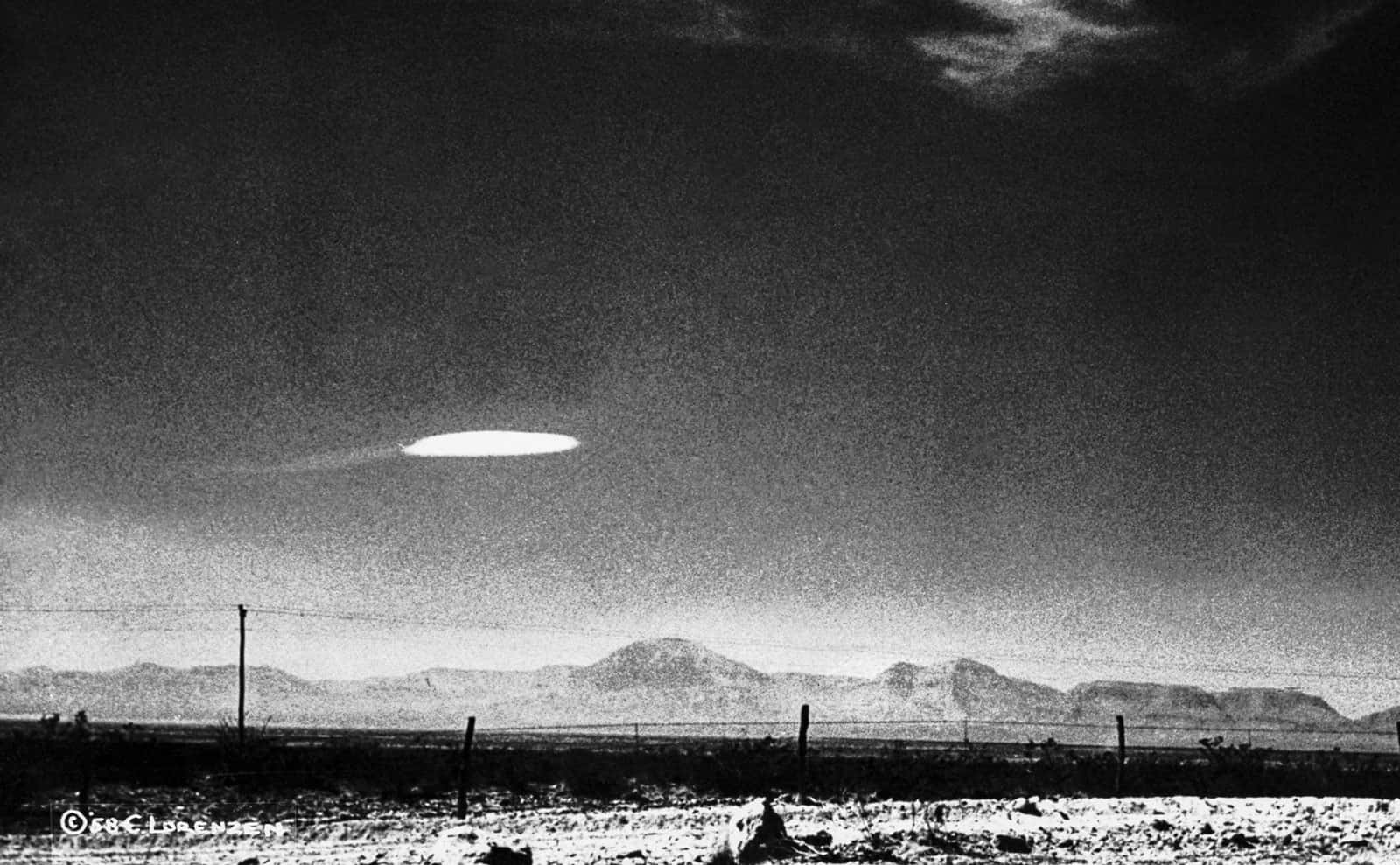 一個發光的UFO懸浮在沙漠上空，遠處有山脈。