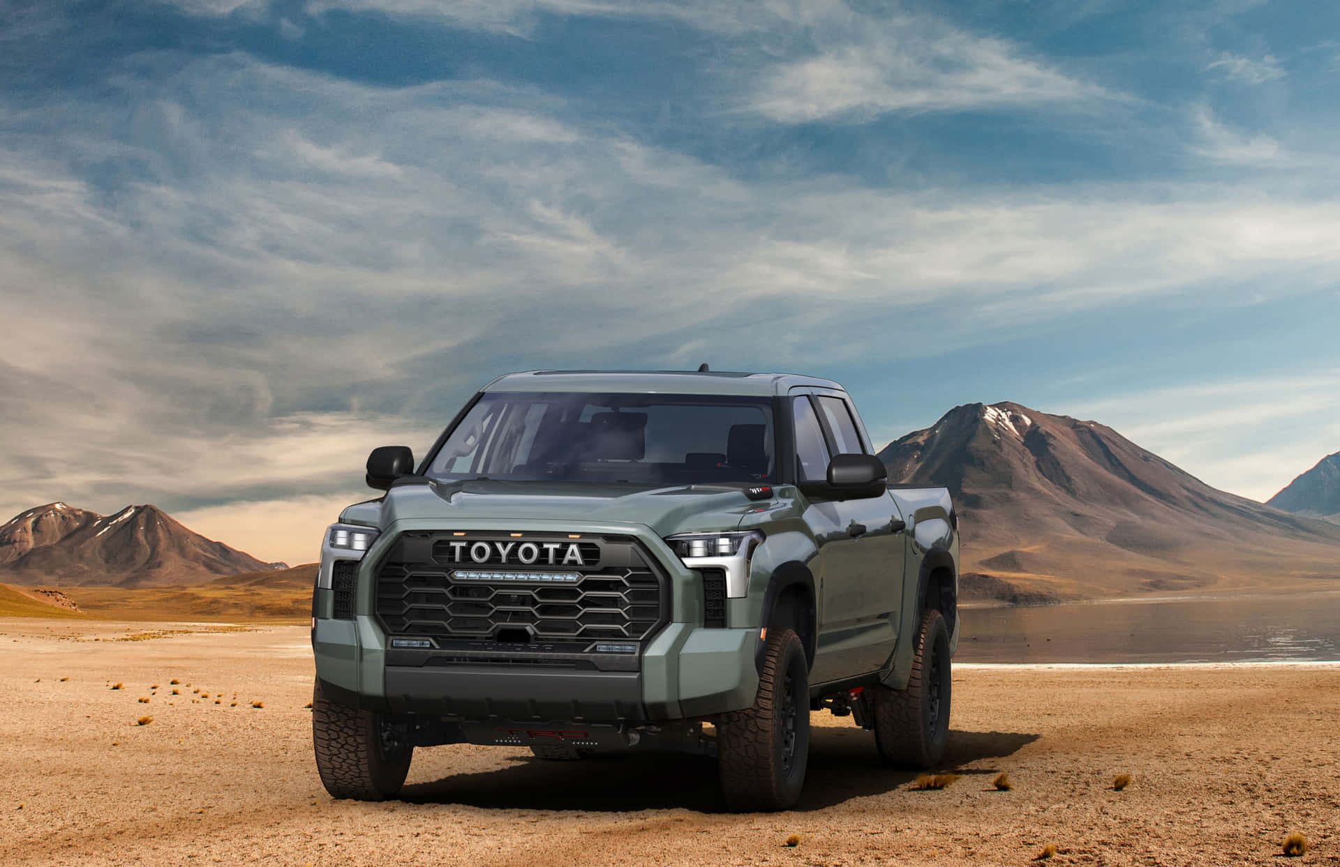 綠色豐田 Tacoma 皮卡車在黃昏時停放在沙漠中，背景有山脈。