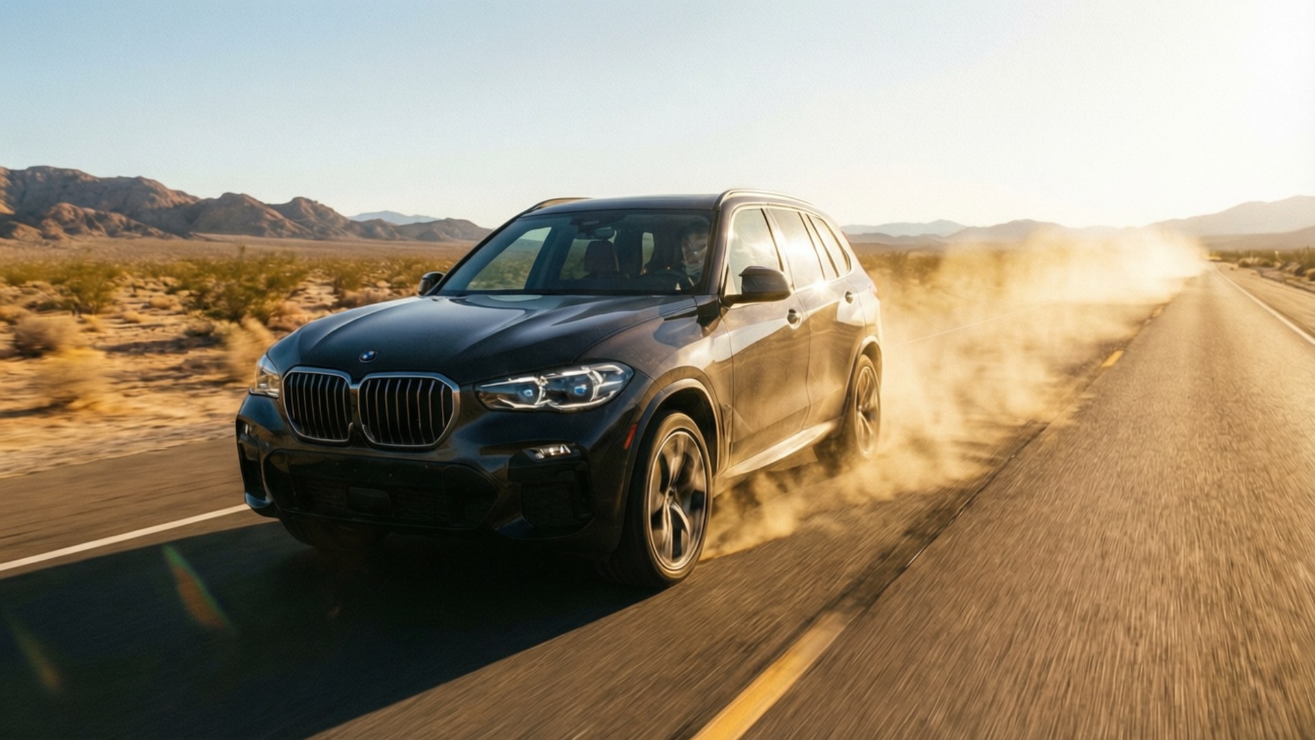 黑色BMW SUV在沙漠公路高速行駛，夕陽下揚起塵土。