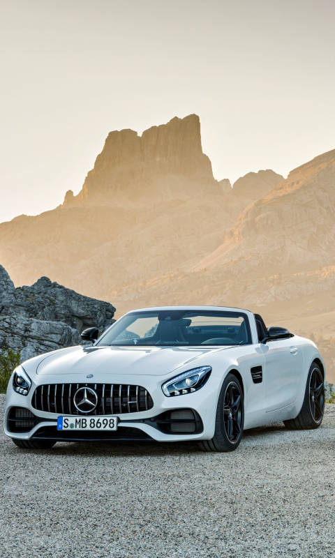白色 Mercedes-AMG GT Roadster 停泊在碎石上，靠近岩石山脈，日落時分。