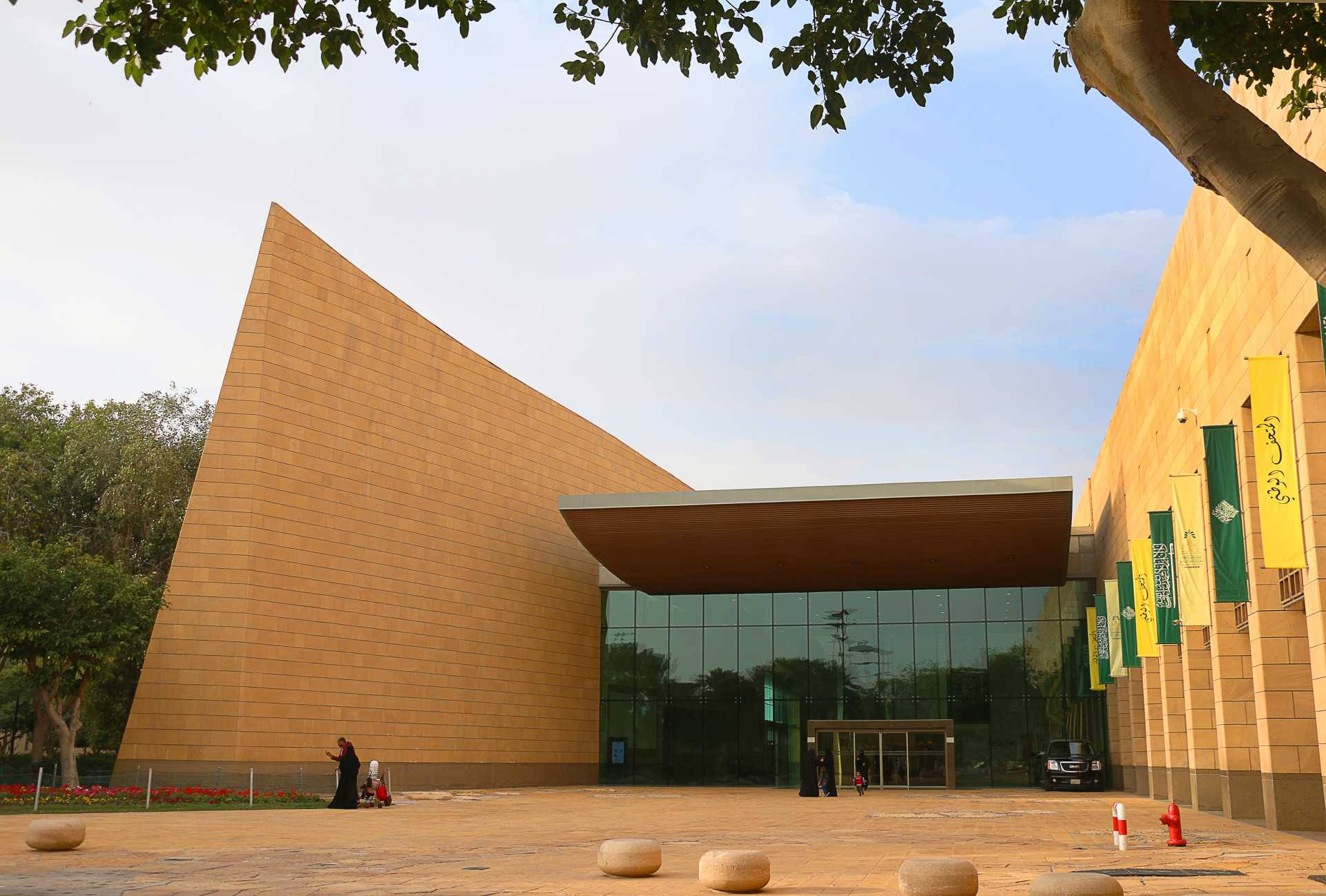 沙特阿拉伯國家博物館 壁紙 — 現代建築奇蹟，金色石牆和玻璃外牆，在樹枝框住的清澈藍天下。