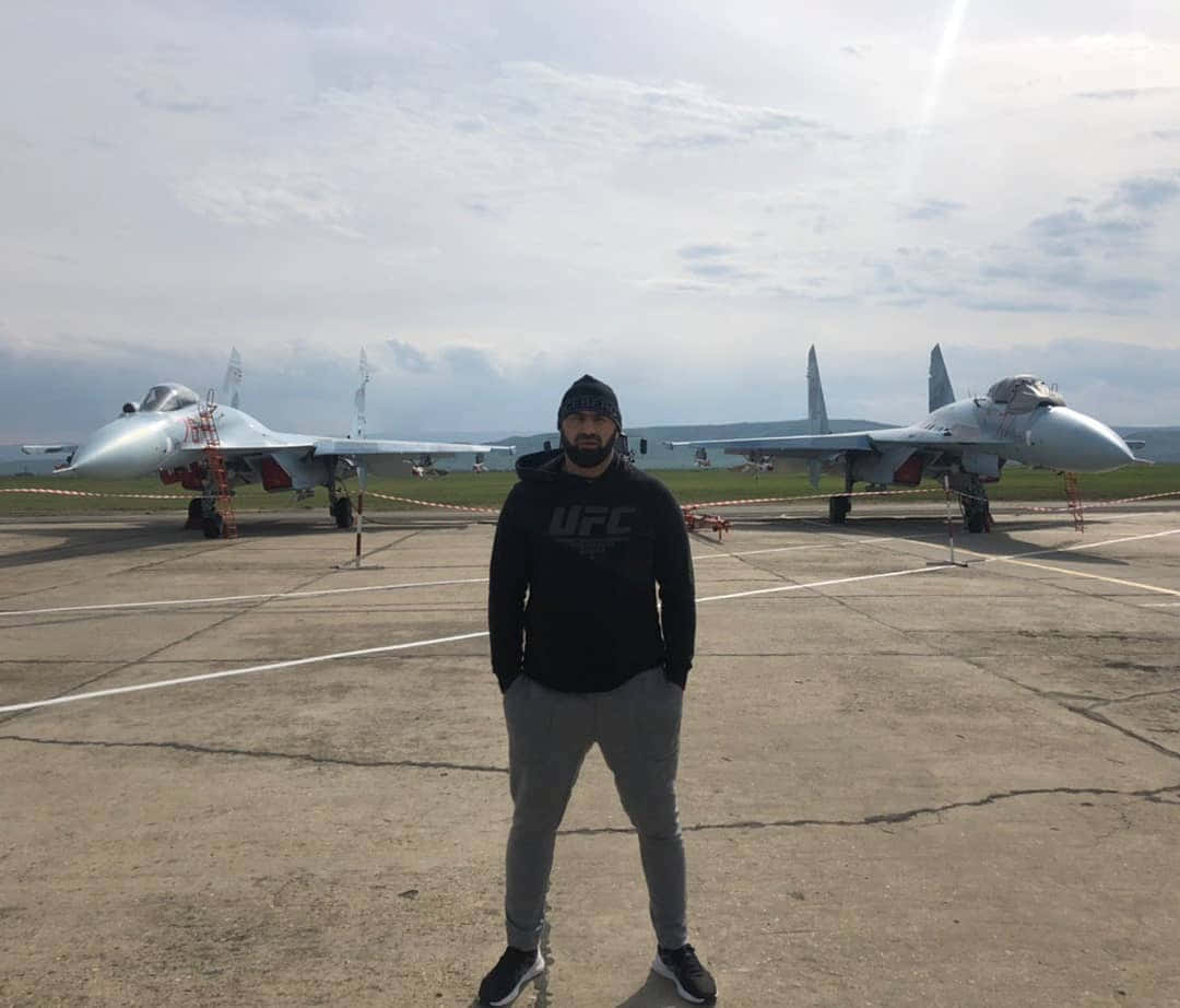 穿著UFC連帽衫的男子站在機場上兩架戰鬥機前。