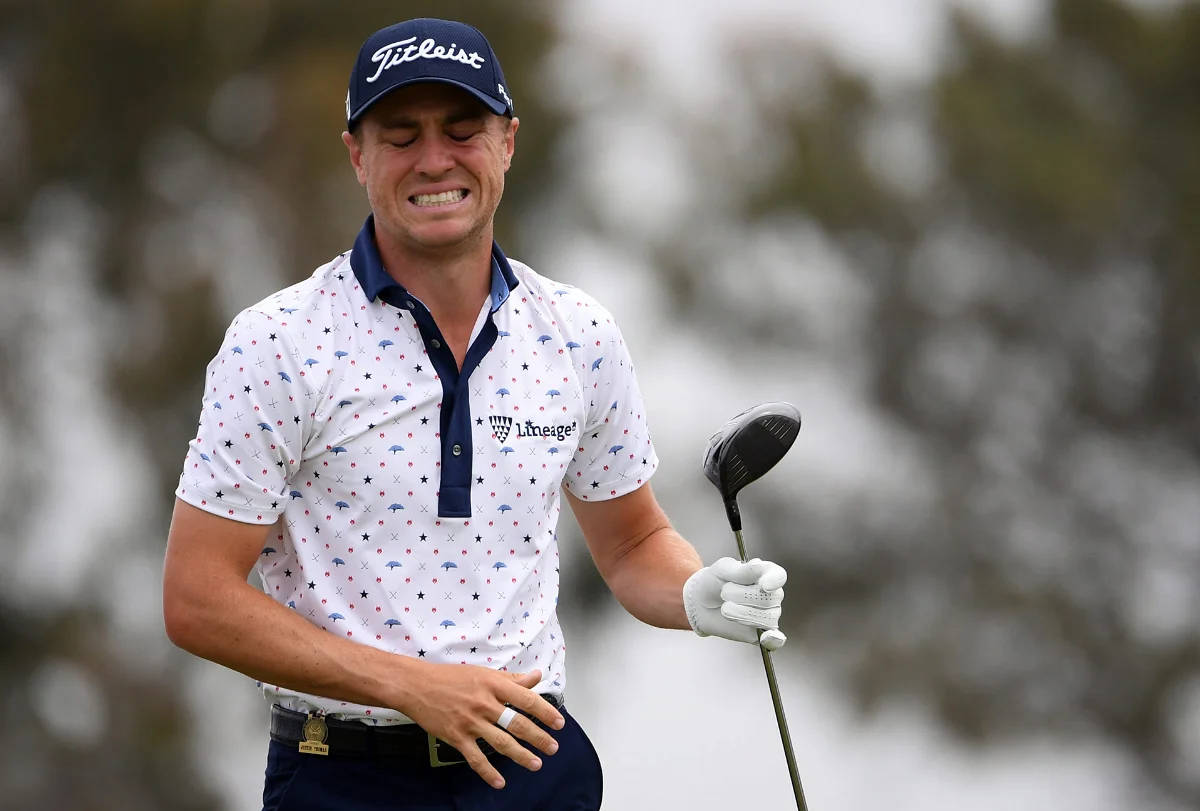沮喪的 Justin Thomas 壁紙 — 一名高爾夫球手在霧氣瀰漫的球場上，身後有模糊的樹木，他握著球杆，沮喪地皺著眉頭。