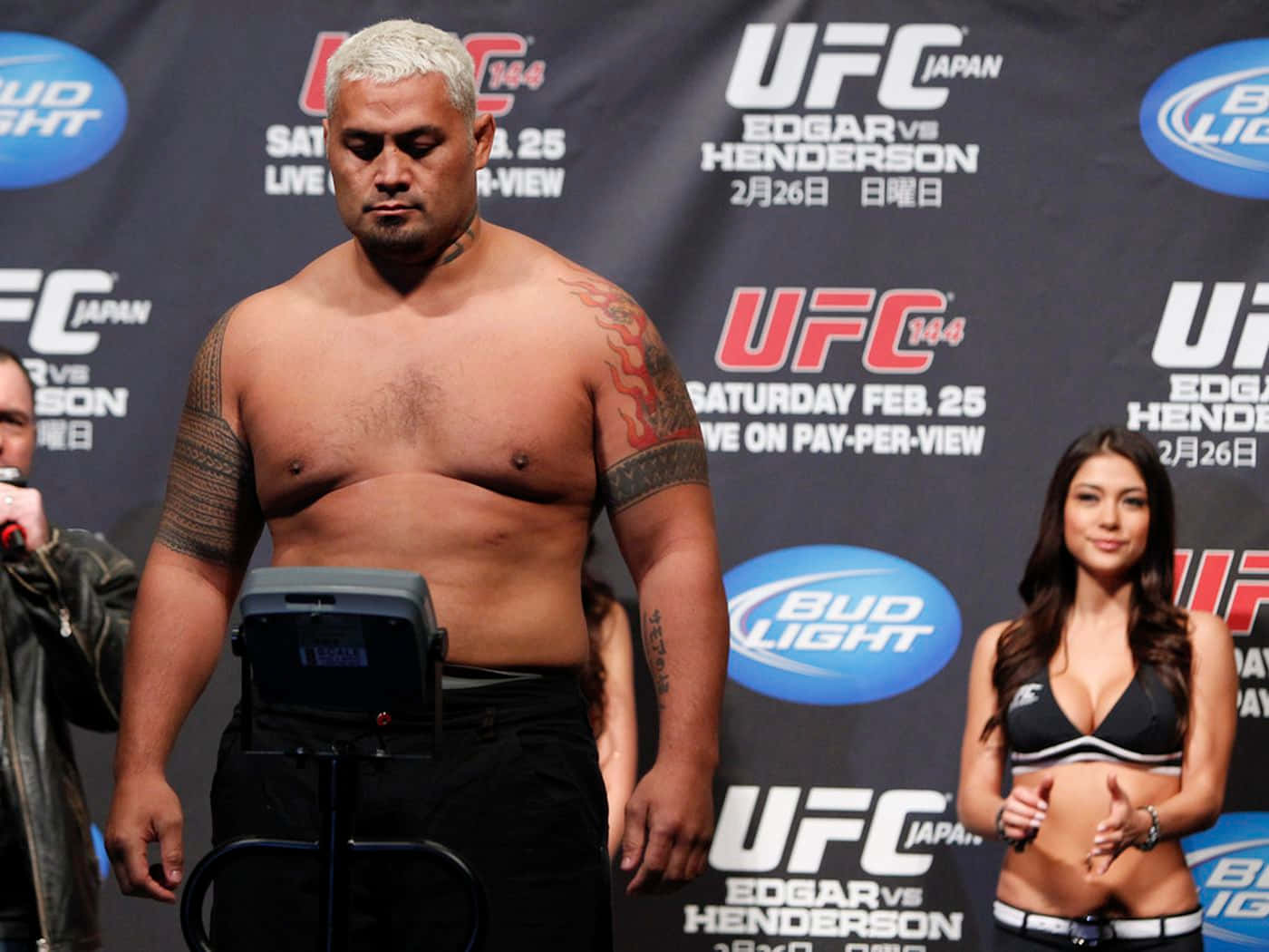 UFC拳手在稱重活動中，身後有宣傳橫幅和舉牌女郎。