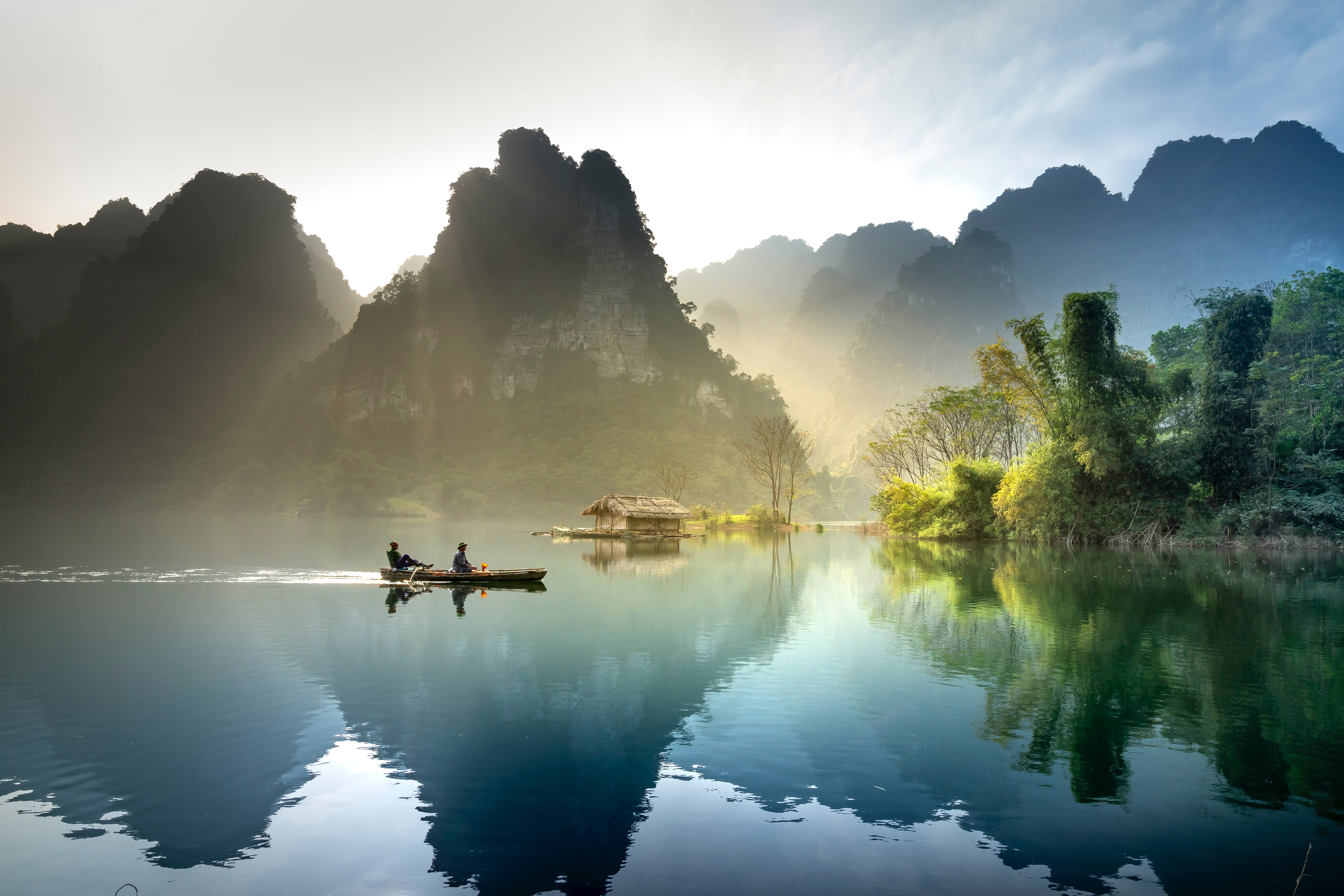 河中島嶼景觀 壁紙 — 日出時分，兩人在霧氣瀰漫的湖上划船，四周是高聳的喀斯特山峰。