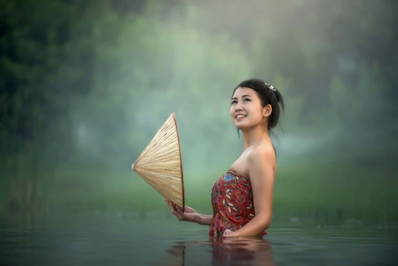 穿著圖案連衣裙的女子手持圓錐形帽子，站在霧氣瀰漫的水中。