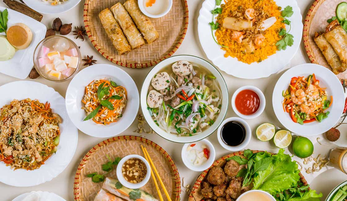 河內最佳美食 壁紙 — 編織墊上色彩繽紛的越南菜餚俯視圖，包括河粉春捲和新鮮香草。