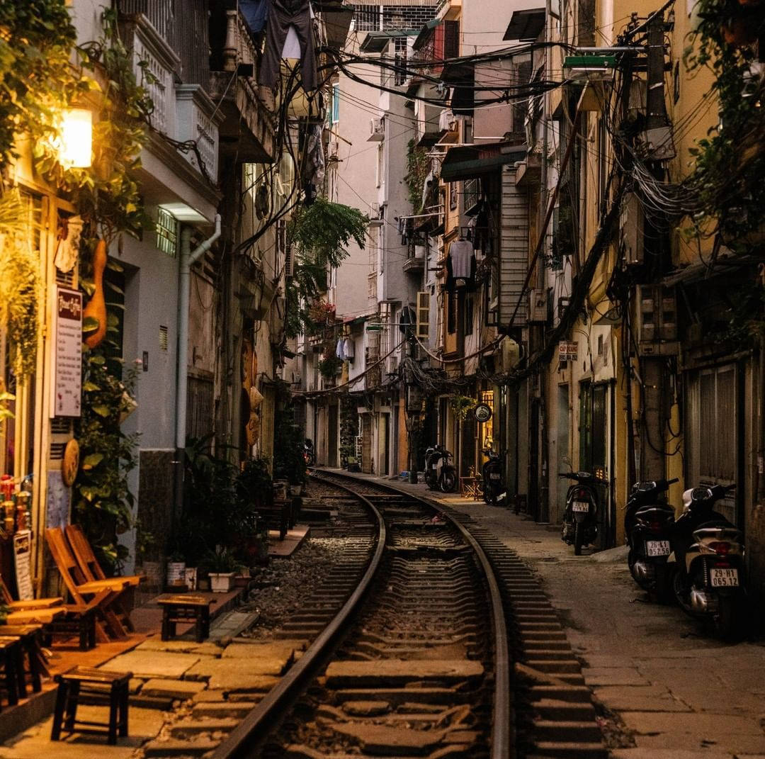 夜晚城市小巷，有鐵路軌道和暖燈下停泊的電單車。