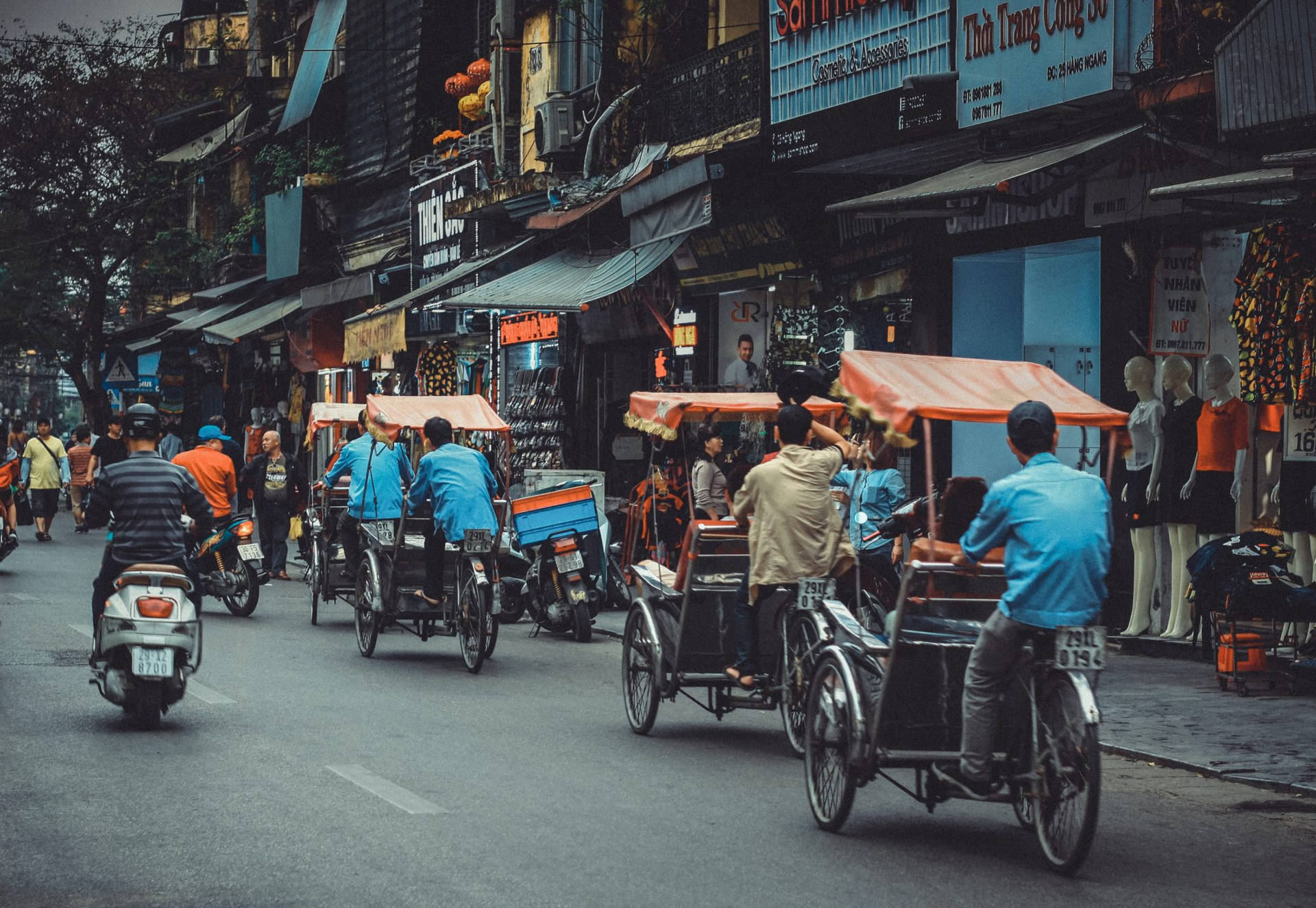 河內繁忙的街道，人力車和摩托車經過商店和人體模型。