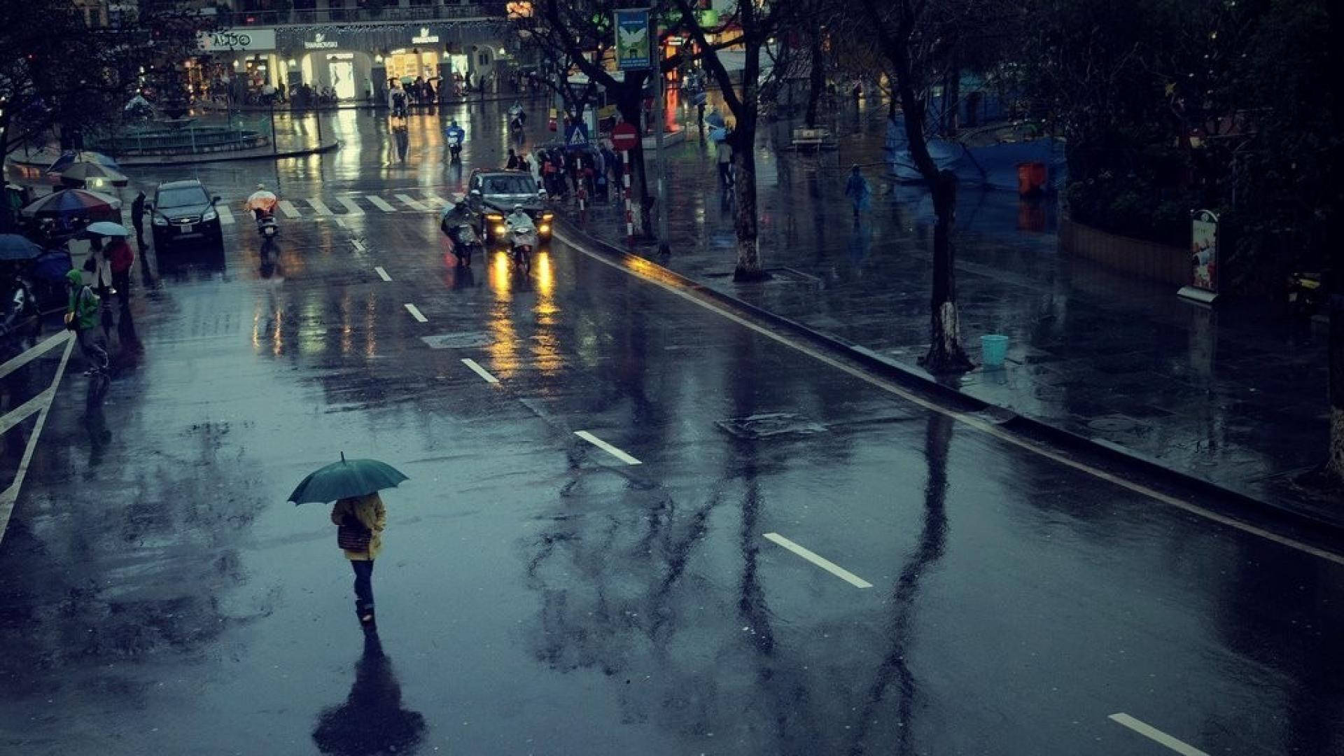 河內雨後潮濕街道 壁紙 — 一個孤獨的身影撐著雨傘，在夜間走過被雨水浸濕的城市街道，車頭燈在濕漉漉的路面上反射。