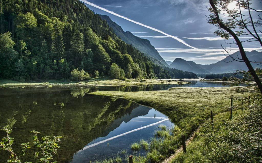 被山脈和森林環繞的寧靜湖泊，清晰的倒影和天空中的飛機軌跡。