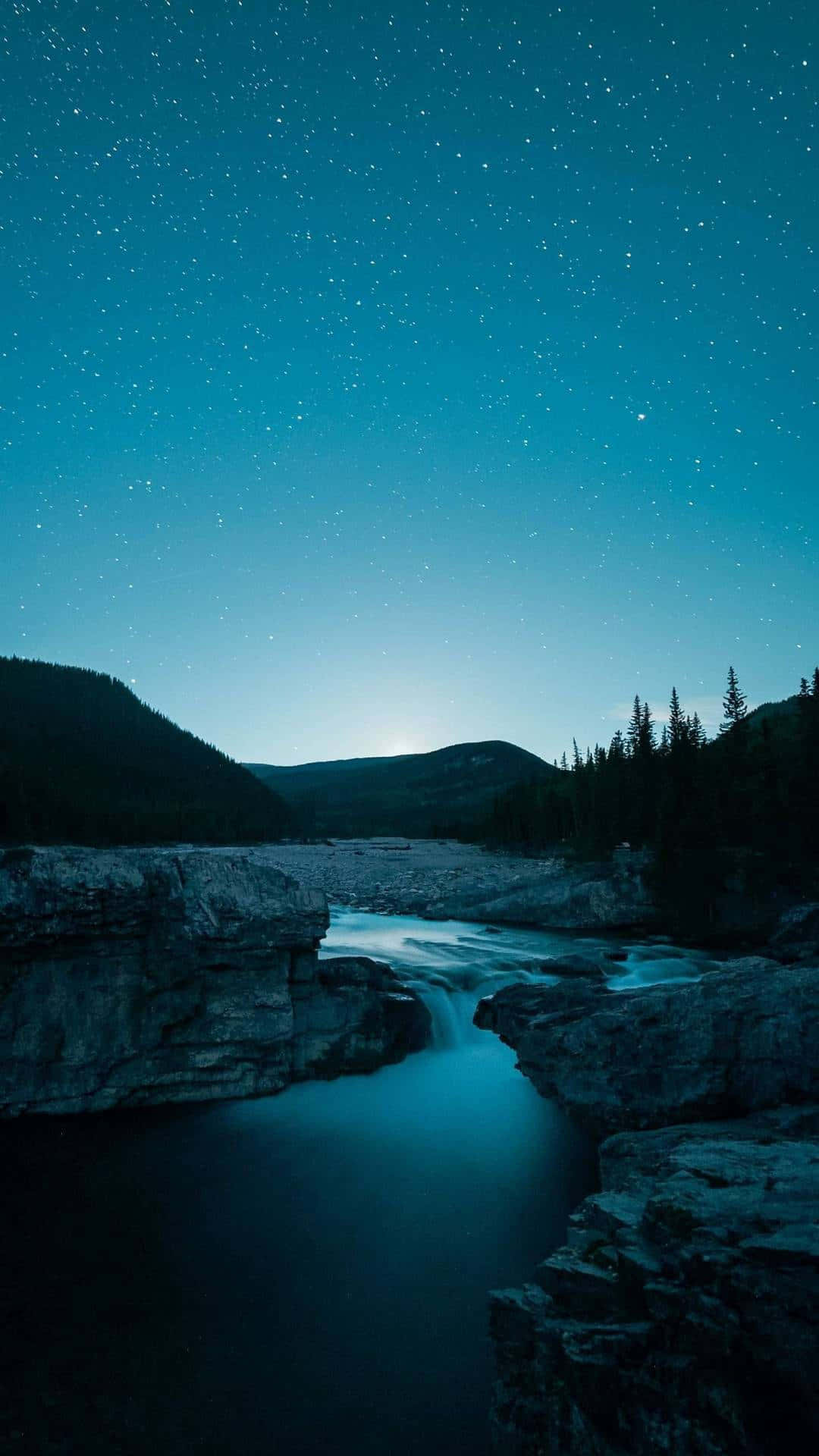 河景超 AMOLED 顯示器 壁紙 — 星空之夜在寧靜的河流上閃耀，流經岩石地形，遠處有山脈和松樹。