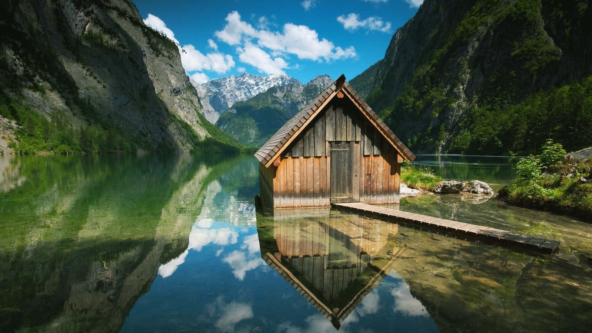木屋漂浮在清澈的山湖上，完美倒映，背景是白雪覆蓋的山峰。