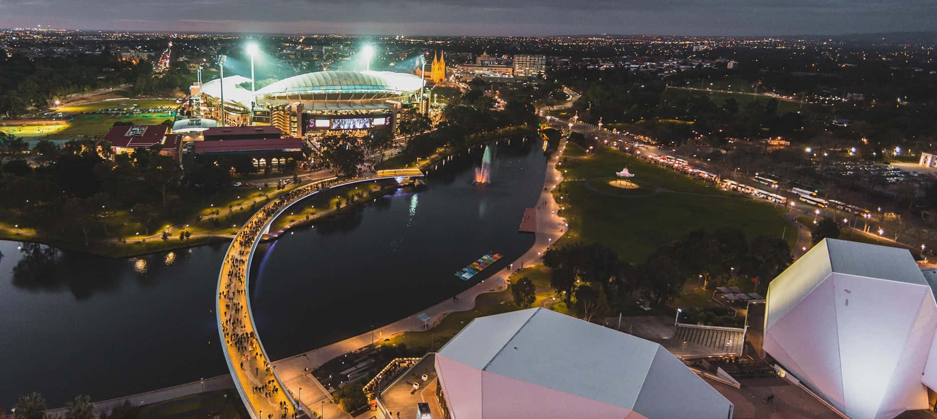 Adelaide 桌布 壁紙 — 河邊發光體育場以及燈光璀璨的橋樑和現代建築的夜間航拍景觀。