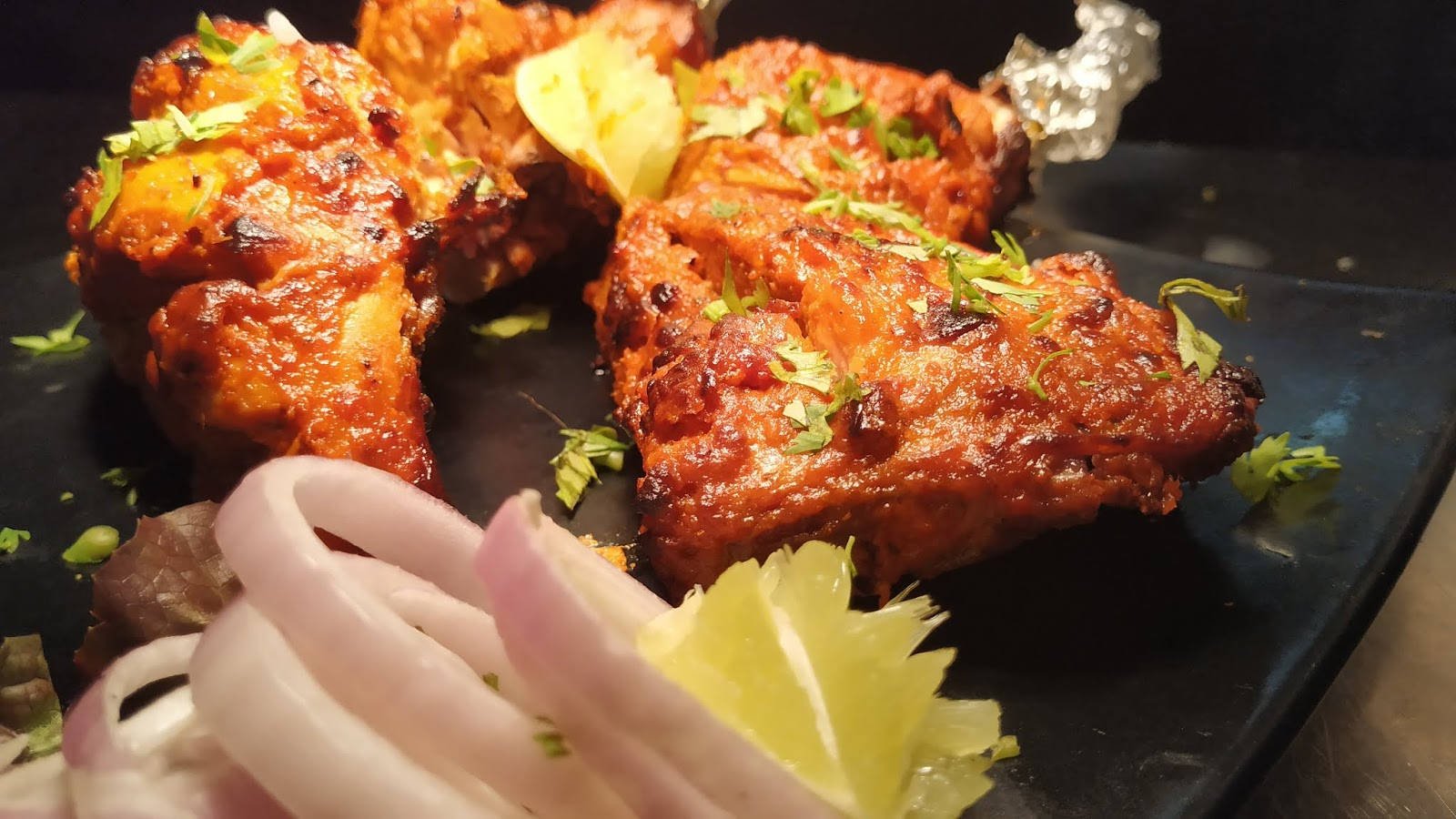 油炸塔多里雞 壁紙 — 酥脆的坦都里雞塊閃耀著香料光澤，在深色盤子上以新鮮香菜和檸檬角裝飾。