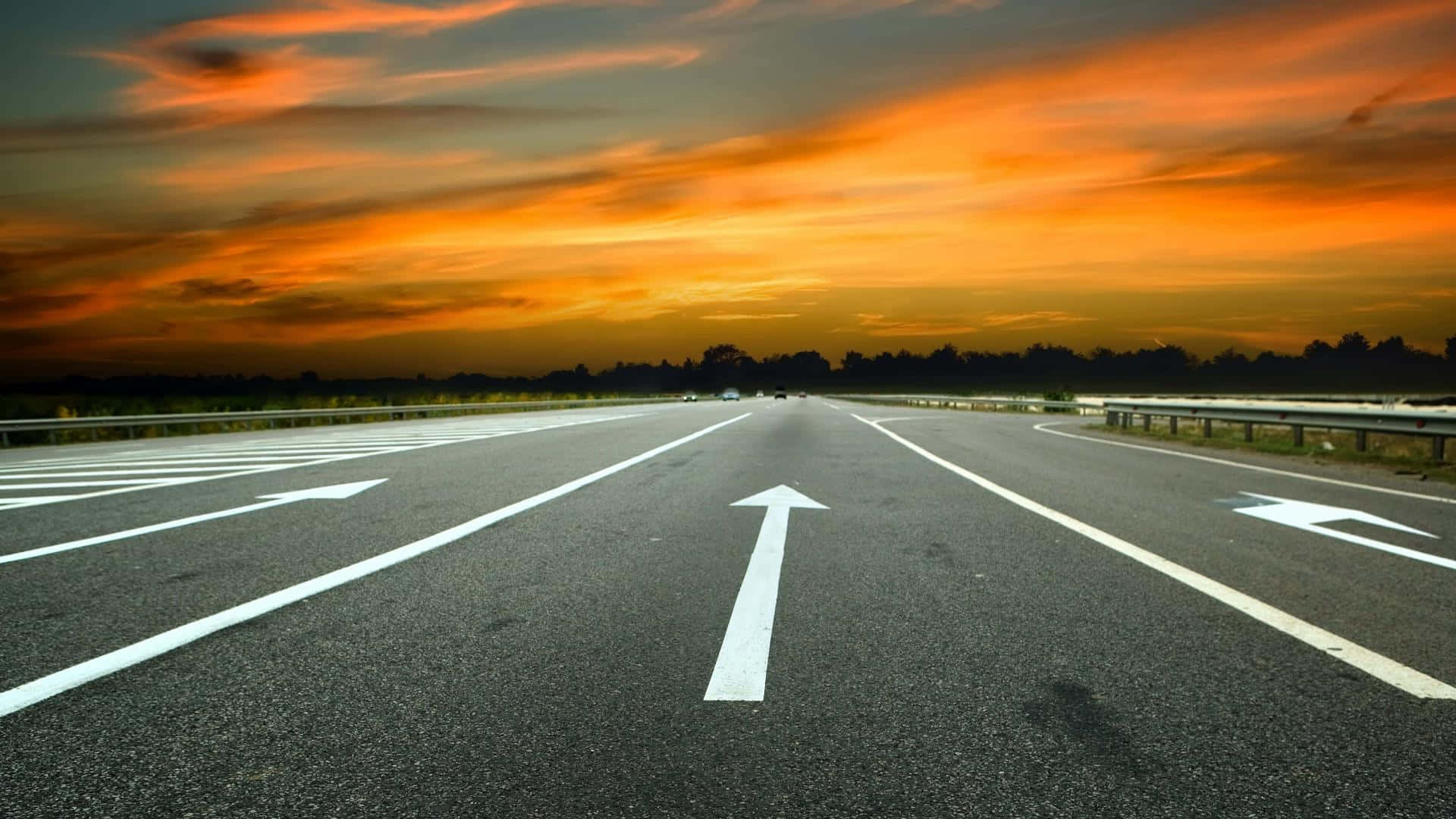 沿開放公路疾馳 壁紙 — 一條寬闊的高速公路在火紅的橙色和紅色日落天空下延伸至地平線。