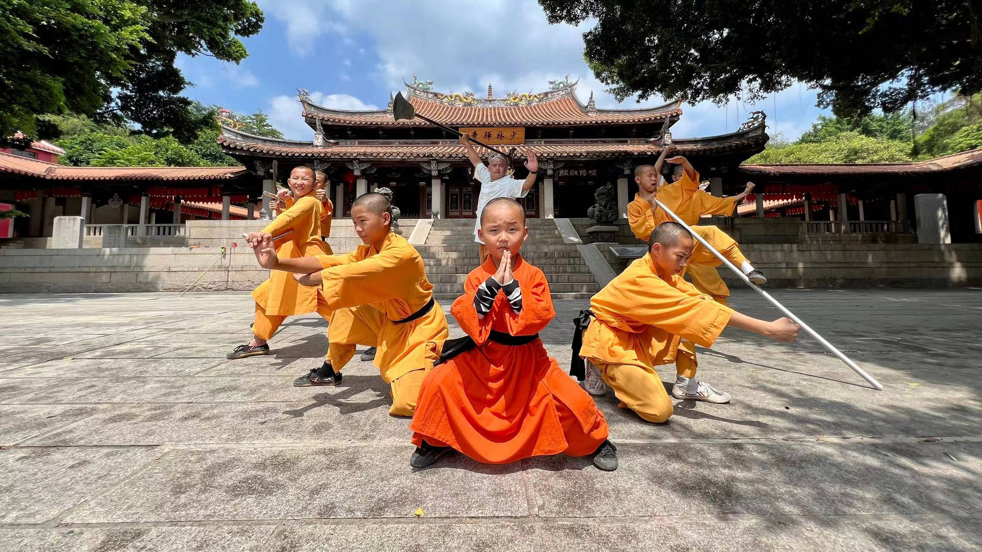 身穿橙色僧袍的年輕僧侶在傳統寺廟前練習武術。