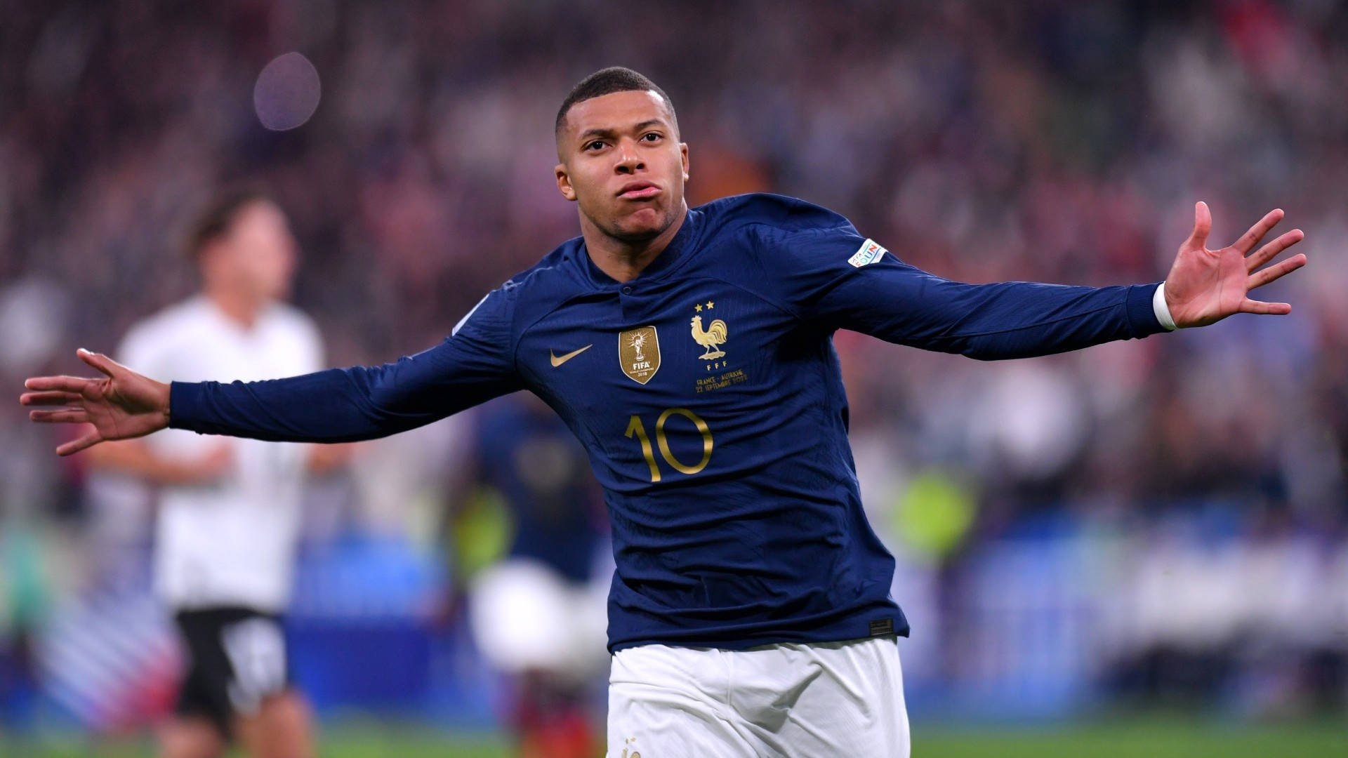 法國國家足球隊基利安·姆巴佩 壁紙 — 一位身穿藍色球衣、背號10的法國足球員在球場上張開雙臂慶祝。