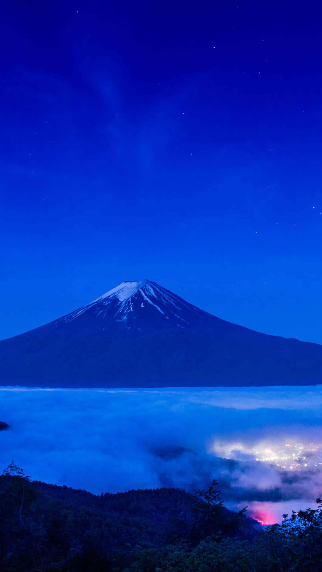 暮色中的富士山，下方有雲和遠處的燈光