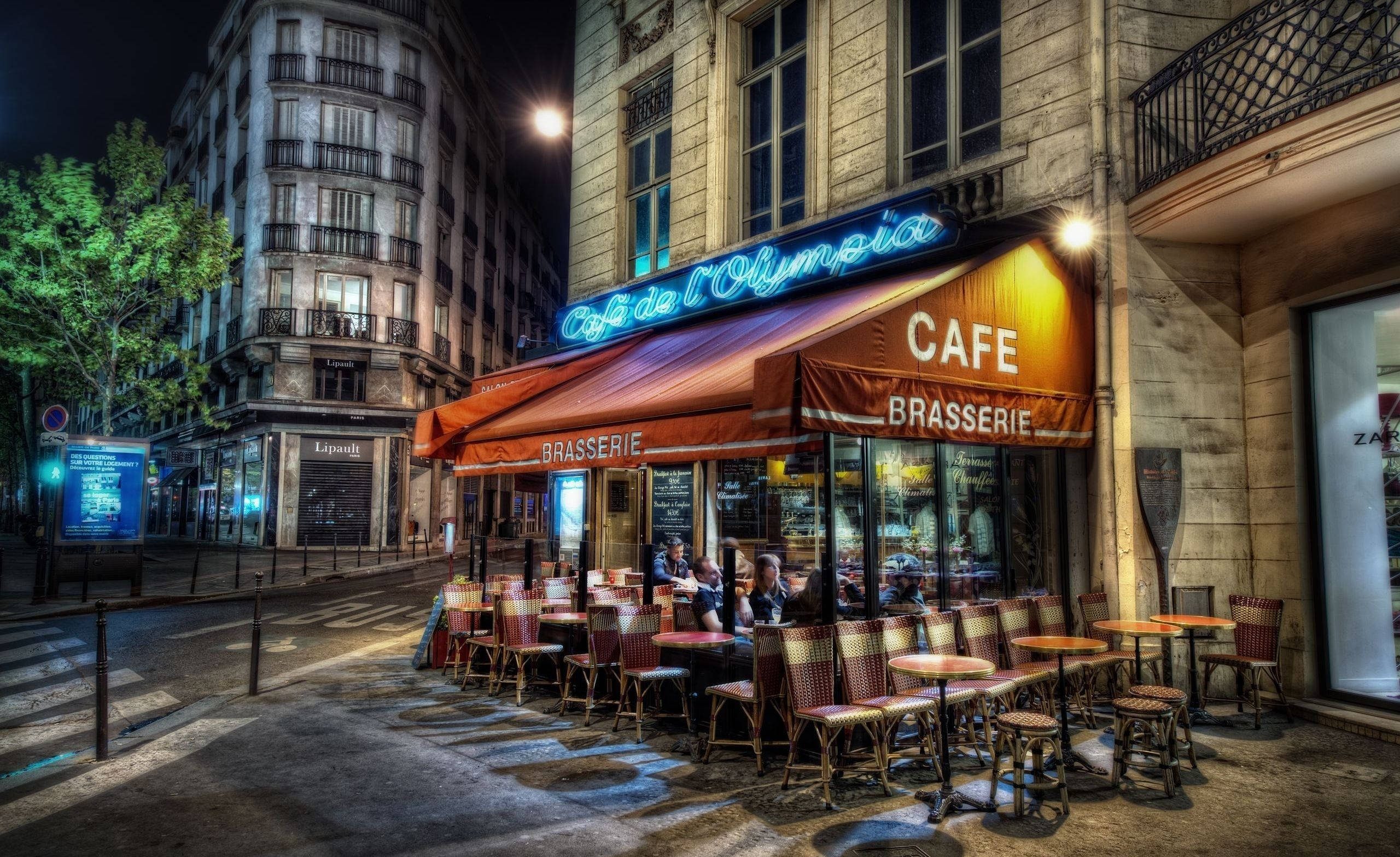 法國巴黎Cafe de Olympia 壁紙 — 夜晚充滿活力的巴黎咖啡館，霓虹燈閃爍，顧客坐在紅色遮陽篷下。