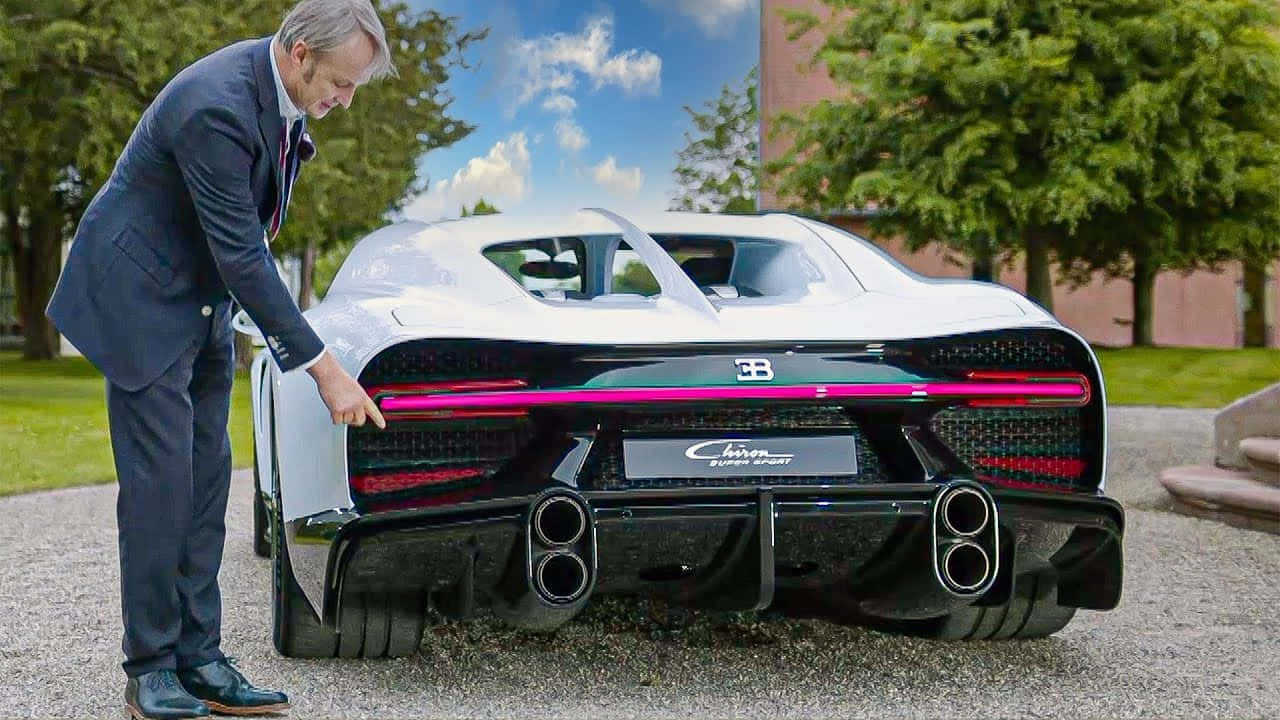 身穿西裝的男子指著碎石車道上白色Bugatti Chiron Super Sport的車尾。