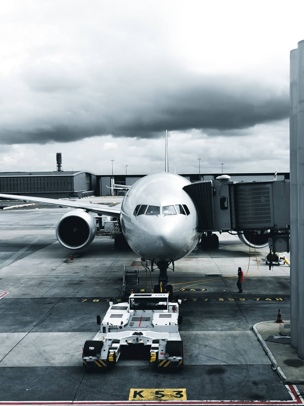 一架大型銀色飛機停泊在機場閘口，有地勤人員和牽引車。