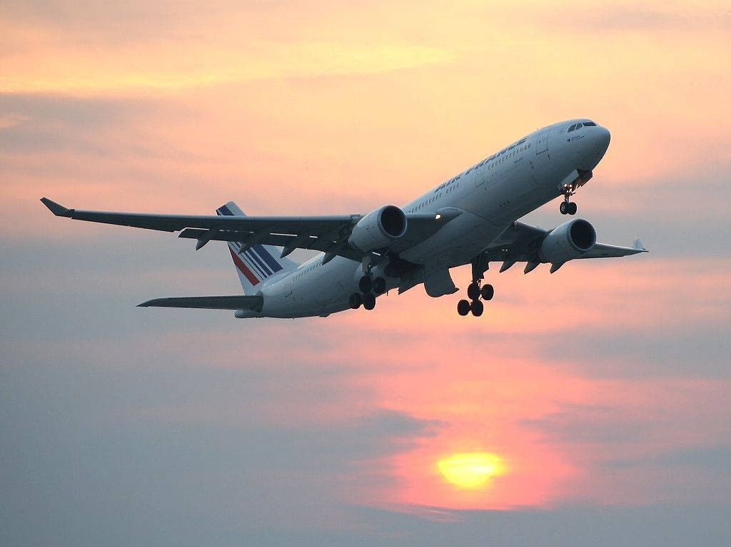 客機在日落時分降落，天空呈現橙粉紅色