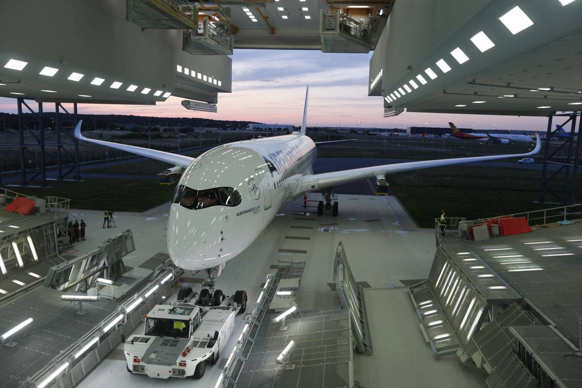 黃昏時機庫內的白色空中巴士A350飛機及地勤人員和車輛。