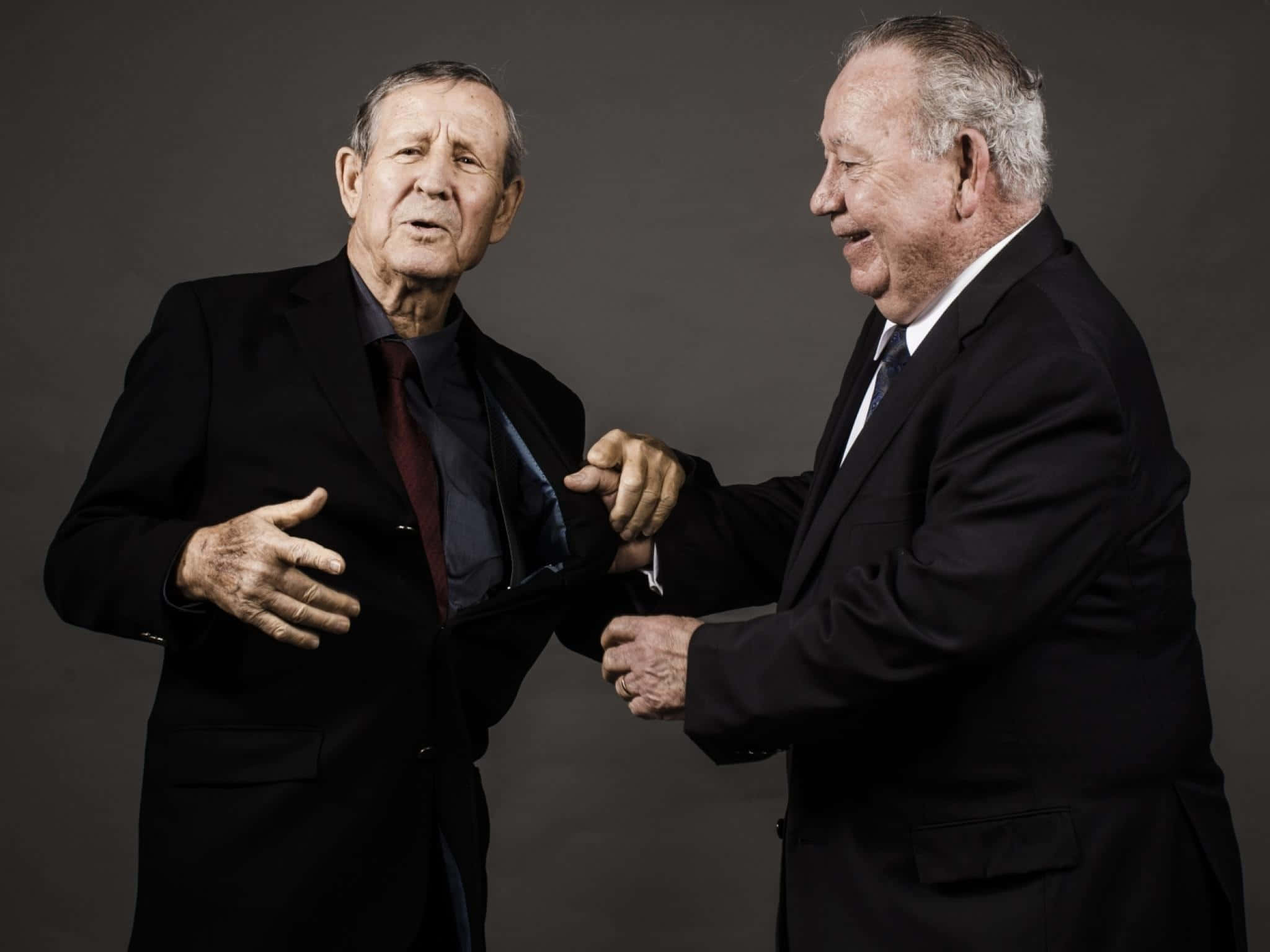 法國足球傳奇Just Fontaine 壁紙 — 兩位身穿深色西裝的長者，在純灰色攝影棚背景下進行嚴肅對話。