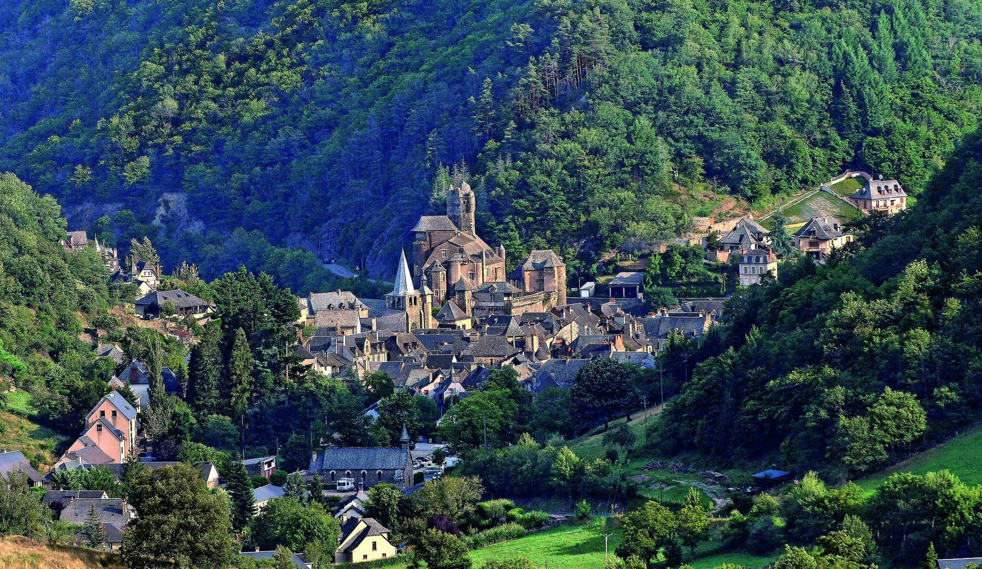 中世紀村莊，有石頭建築和教堂，坐落在綠色山丘中。