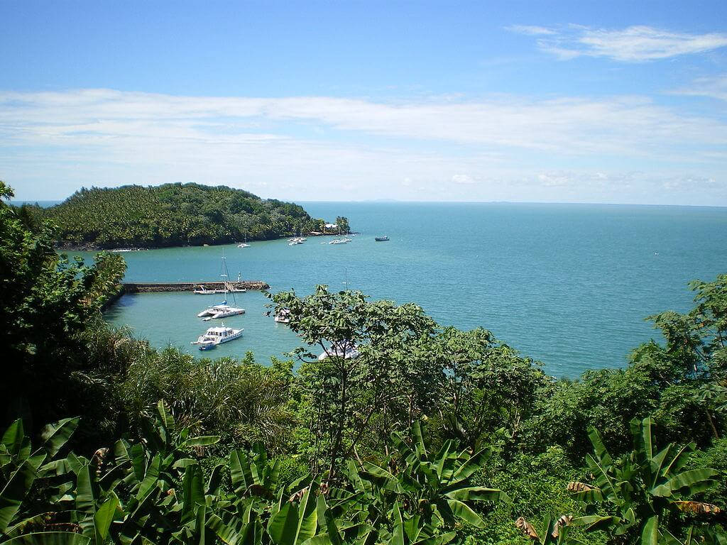 法屬圭亞那皇家島 壁紙 — 一個熱帶海灣，碧綠的海水與白色船隻點綴其間，四周環繞著茂密的綠色叢林，上方是明亮的藍天。