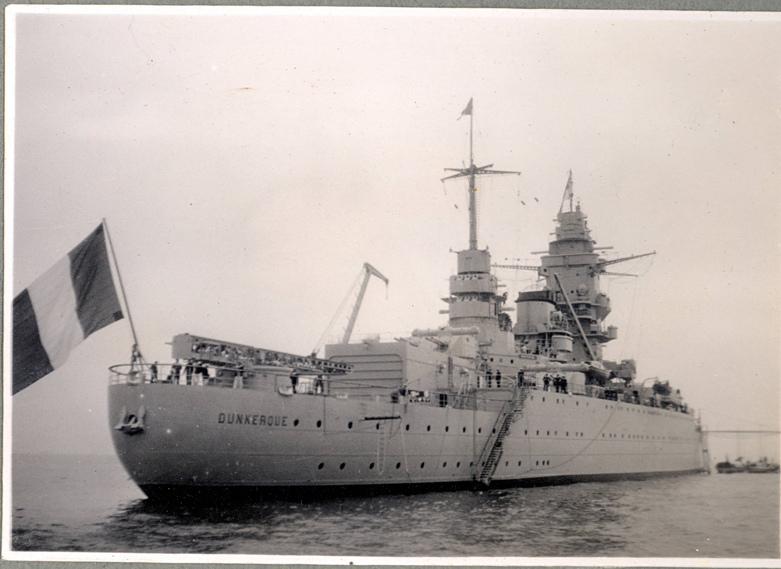 法屬波利尼西亞敦克爾克號艦艇 壁紙 — 一艘歷史悠久的法國戰艦敦克爾克在平靜的水面上漂浮，旗幟飄揚，甲板上可見船員。