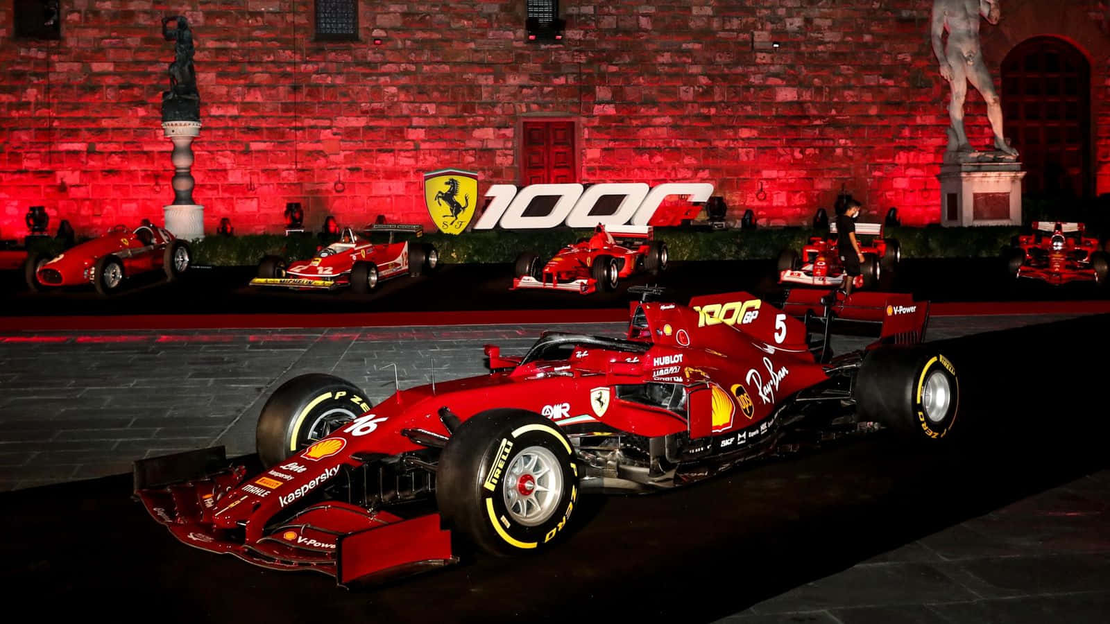 紅色法拉利F1賽車在夜間展示，前面是發光的磚牆，上面有「100」和躍馬標誌。