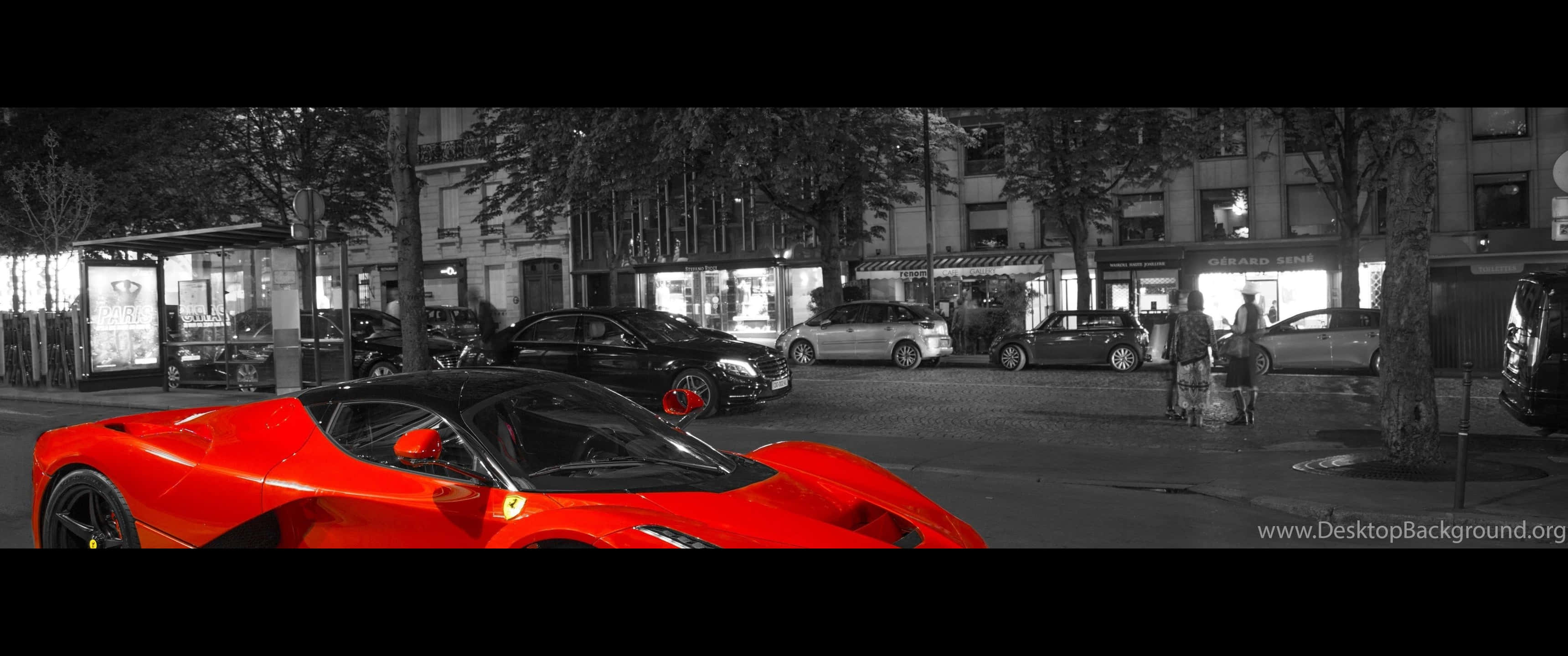 「法拉利速度與風格」 壁紙 — 一輛鮮紅色跑車在夜晚的黑白城市街道上脫穎而出，背景有行人和商店門面。