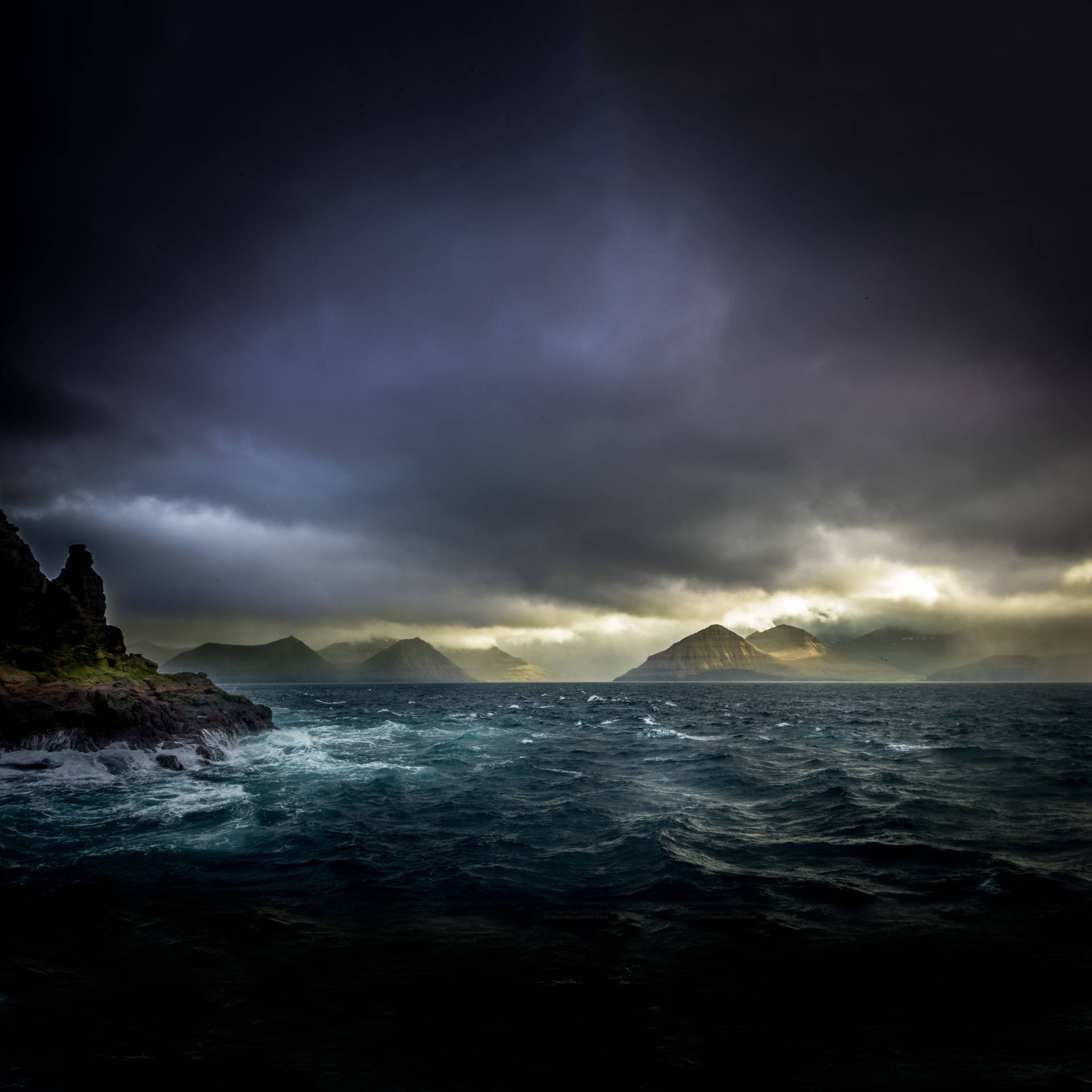 黑暗暴風雨中的海洋，波浪撞擊懸崖，陰沉天空下遠山透過雲層發光。