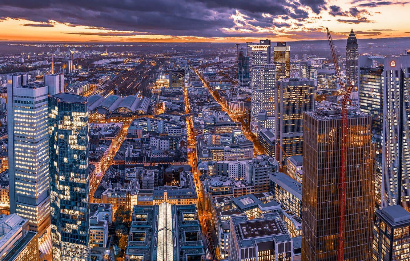Germany 桌布 壁紙 — 法蘭克福天際線在日落時的鳥瞰圖，在戲劇性的紫橙色雲層下，摩天大樓和發光的街道被照亮。