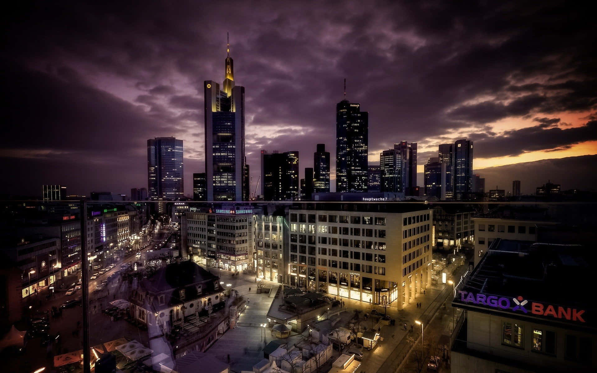 Germany 桌布 壁紙 — 法蘭克福戲劇性的黃昏城市景觀，摩天大樓在紫色和橙色的天空下閃耀著燈光。