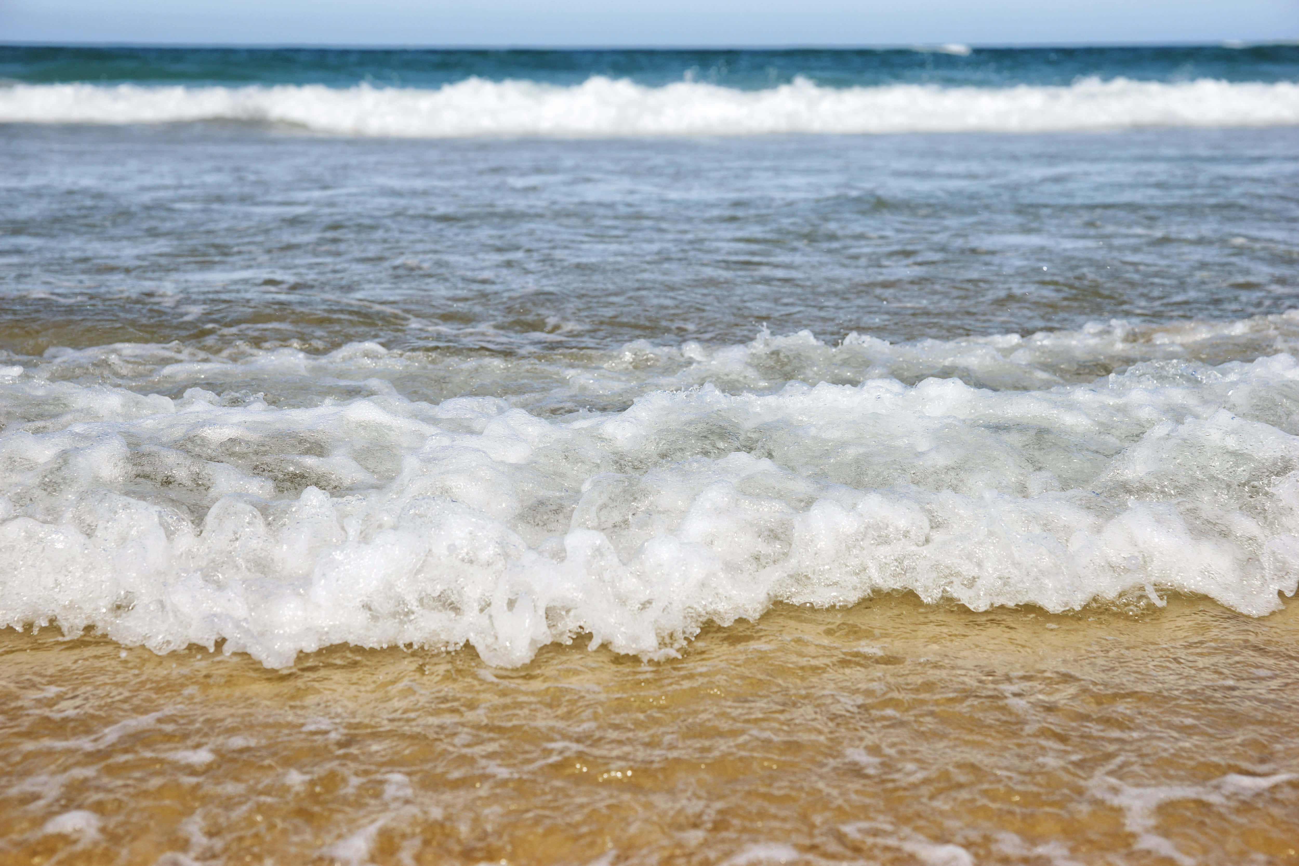 Beach Waves 桌布 壁紙 — 泡沫海浪拍打金色沙灘，在明亮的日光下，上方是清澈的藍天。