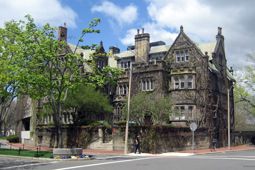 歷史石建築，爬滿常春藤，前面有樹木和街道。