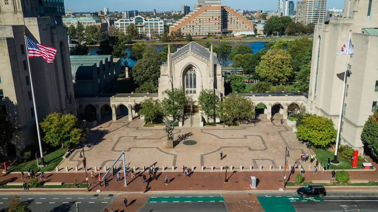 波士頓大學神學系大樓晴空下 壁紙 — 大學校園廣場的鳥瞰圖，設有哥德式教堂、美國國旗，學生在晴朗藍天下行走。