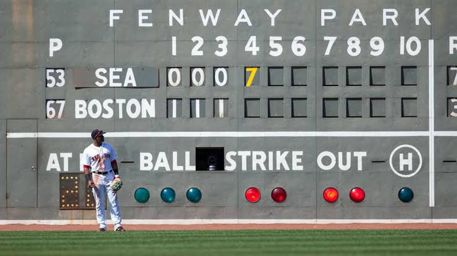 波士頓紅襪對戰西雅圖水手隊MLB比分 壁紙 — 一名棒球選手站在芬威球場標誌性的手動計分板前，顯示波士頓在第七局以7-0領先西雅圖。